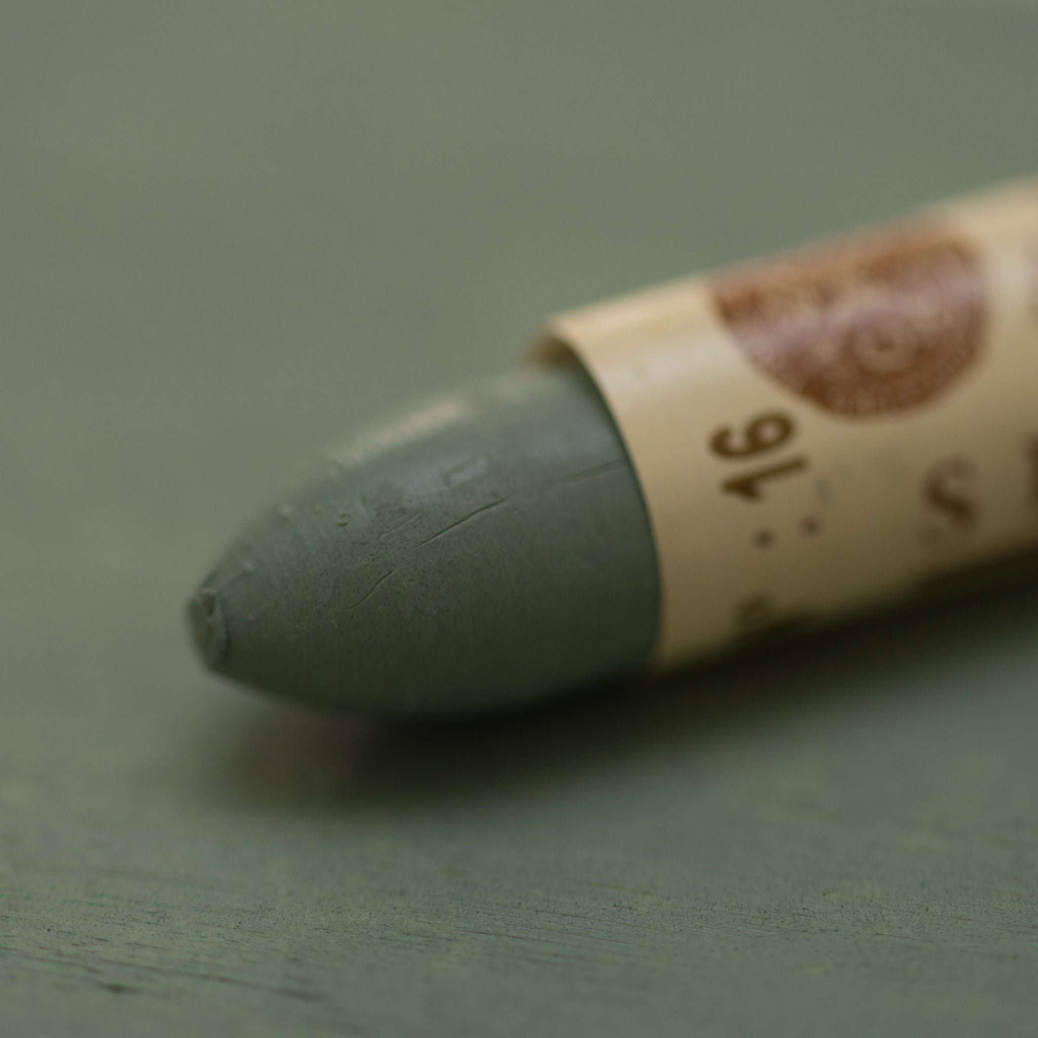 A close-up of a Sennelier oil pastel on a Green-Grey background.