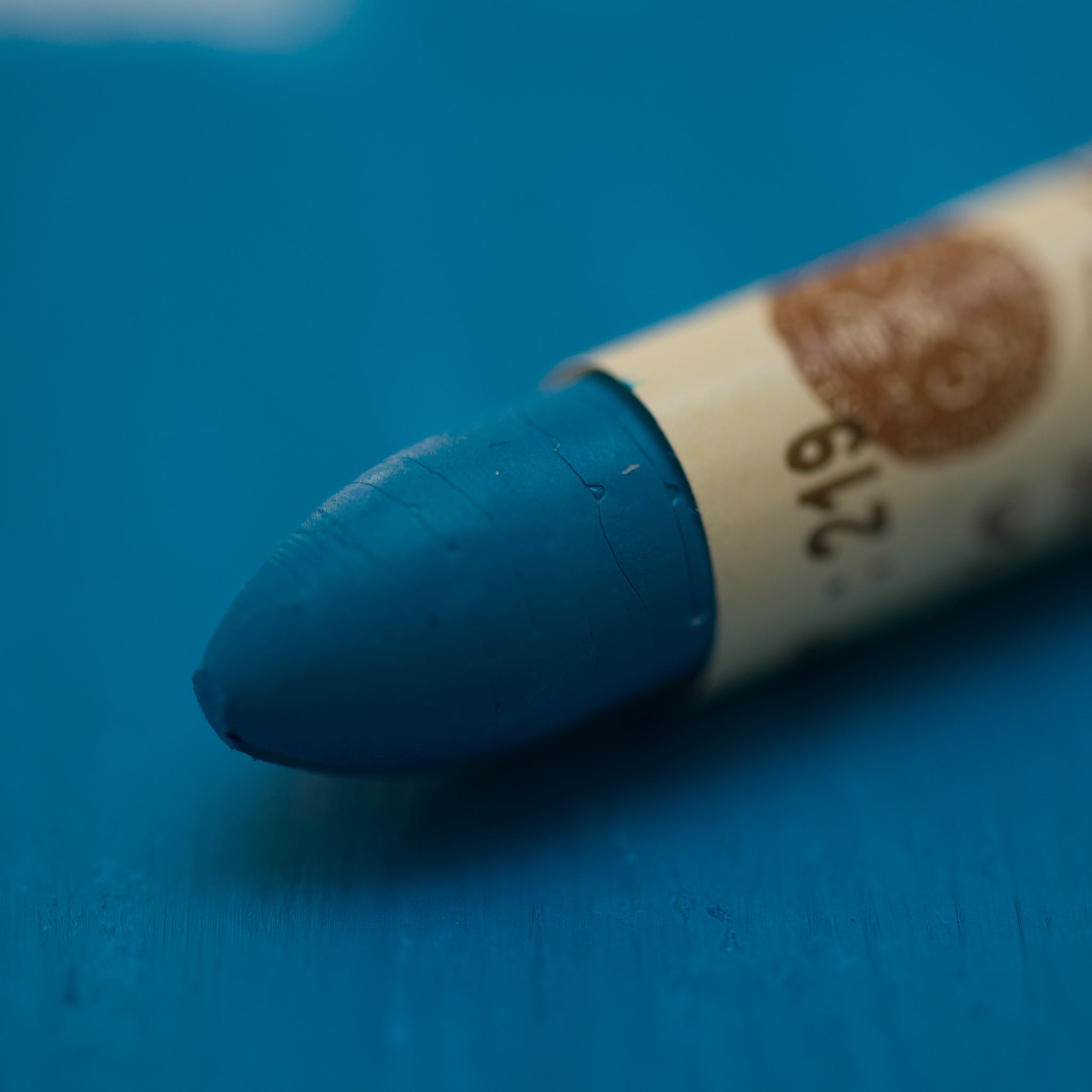 A close-up of a Sennelier oil pastel on a  blue background.
