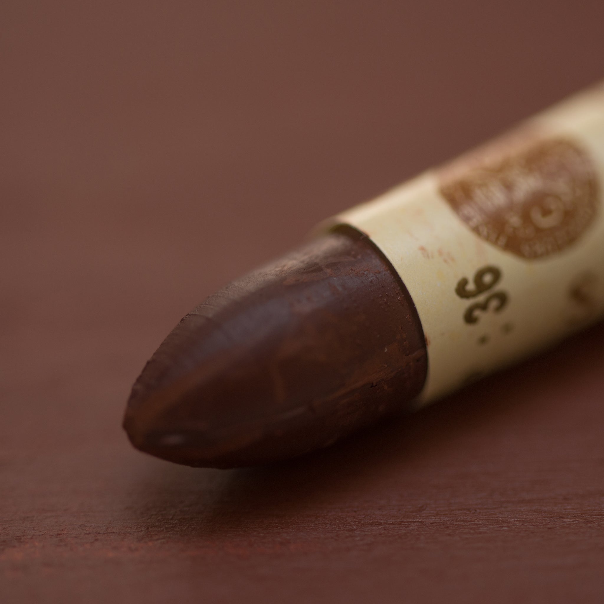 A close-up of a Sennelier oil pastel on a brown background.