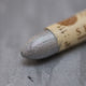 A close-up of a Sennelier oil pastel on a mettalic grey background.