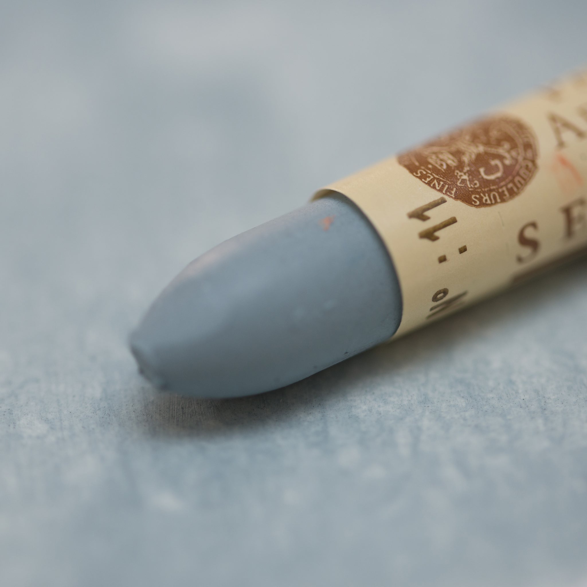 A close-up of a Sennelier oil pastel on a grey background.