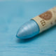 A close-up of a Sennelier oil pastel on a metallic blue background.
