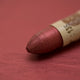 A close-up of a Sennelier oil pastel on a metallic red background.