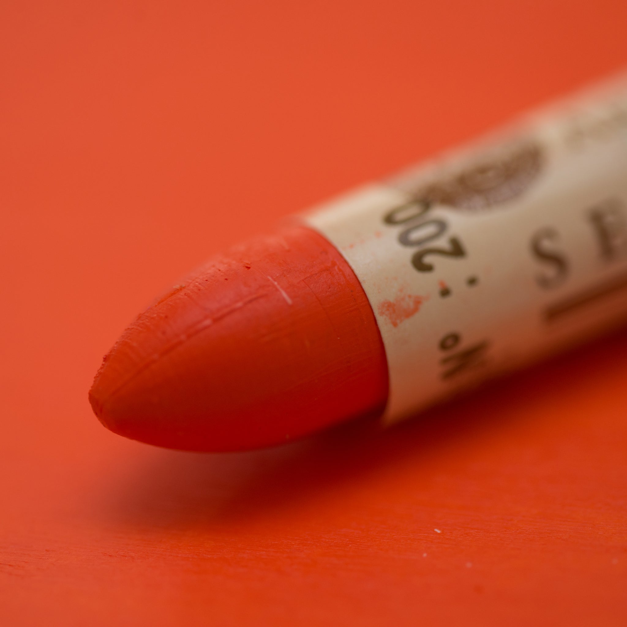 A close-up of a Sennelier oil pastel on a  red background.