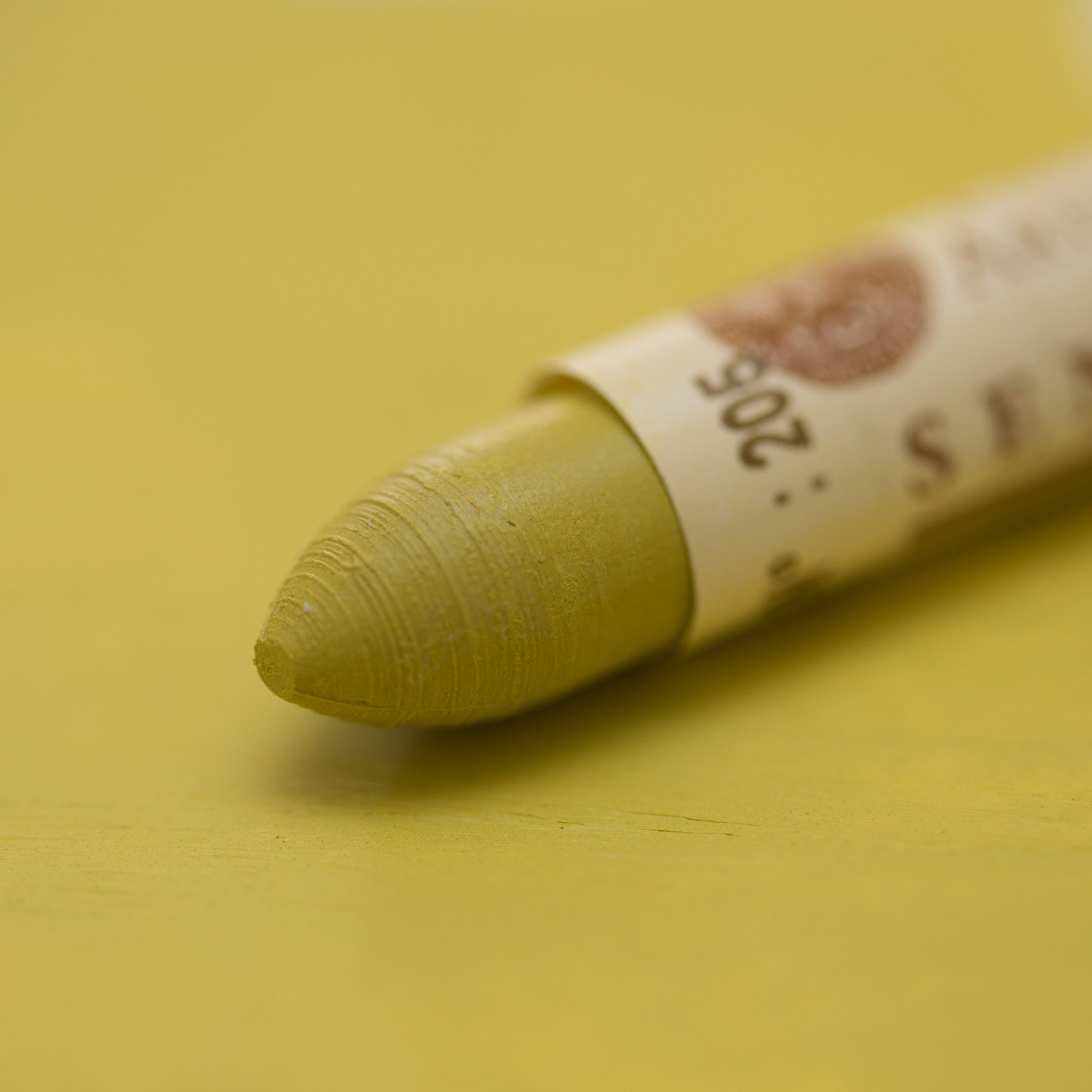A close-up of a Sennelier oil pastel on a  green background.