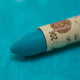A close-up of a Sennelier oil pastel on a  turquoise background.