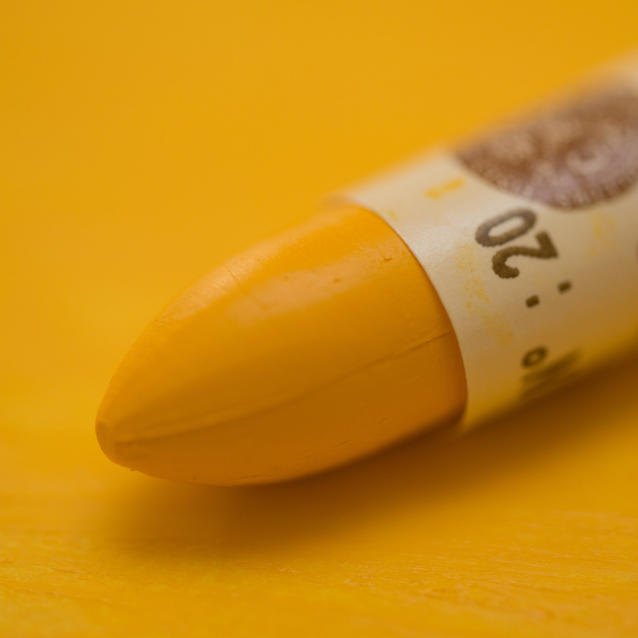 A close-up of a Sennelier oil pastel on a   yellow background.