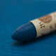 A close-up of a Sennelier oil pastel on a   blue background.