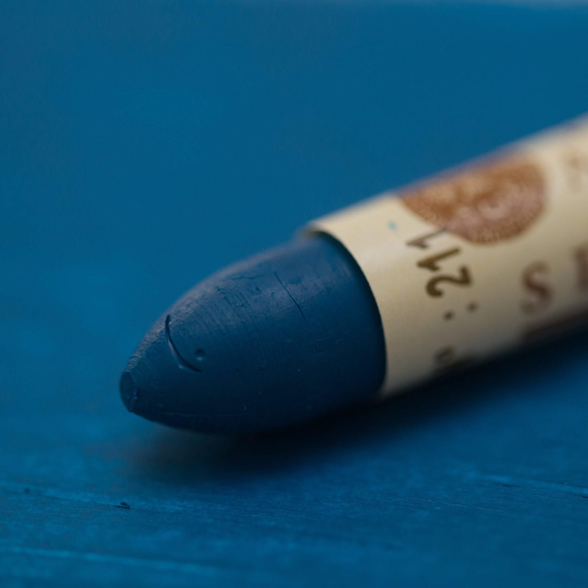 A close-up of a Sennelier oil pastel on a   blue background.