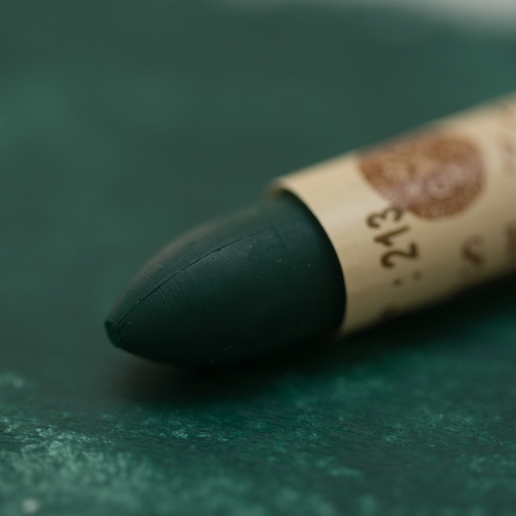 A close-up of a Sennelier oil pastel on a  green background.