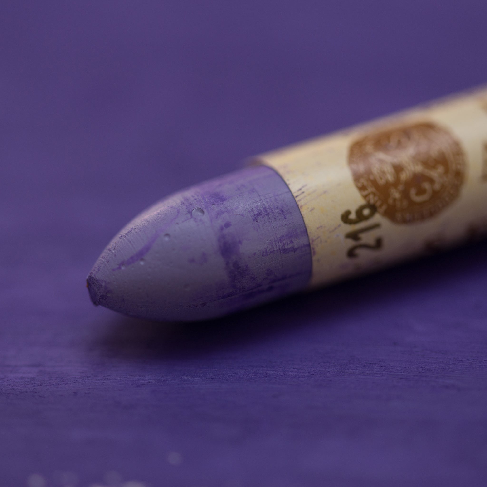A close-up of a Sennelier oil pastel on a  purple background.