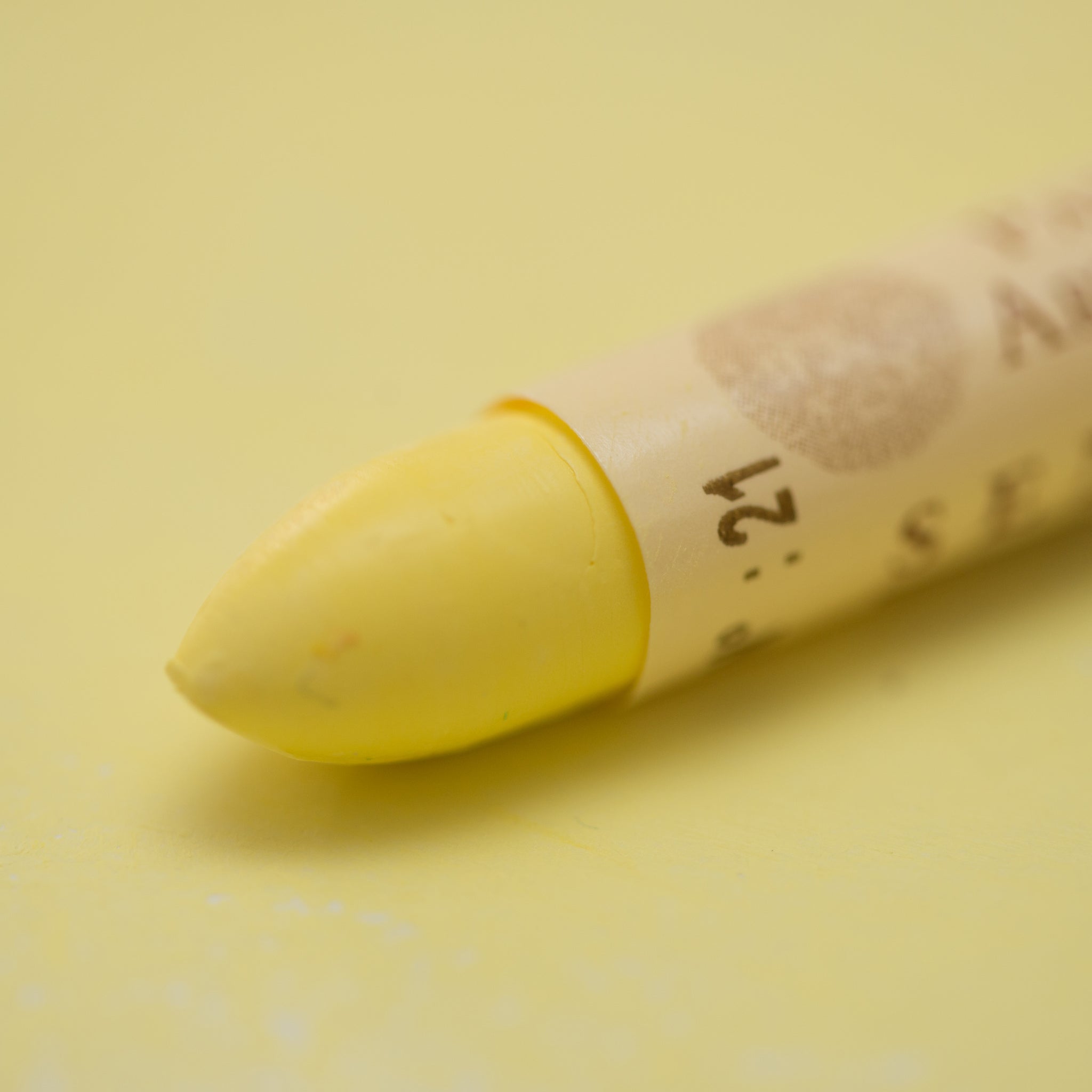 A close-up of a Sennelier oil pastel on a  yellow background.