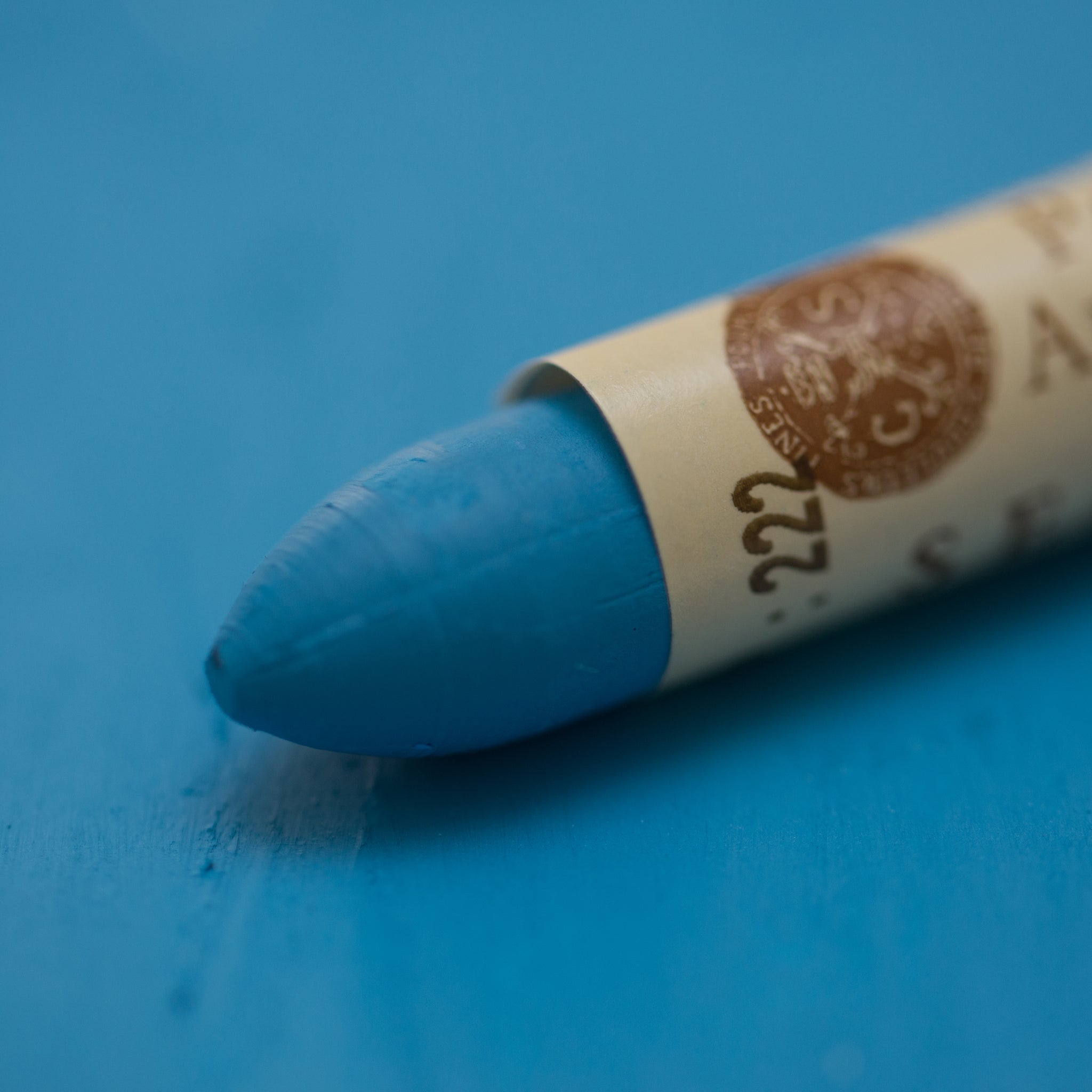 A close-up of a Sennelier oil pastel on a blue background.