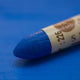 A close-up of a Sennelier oil pastel on a  blue background.