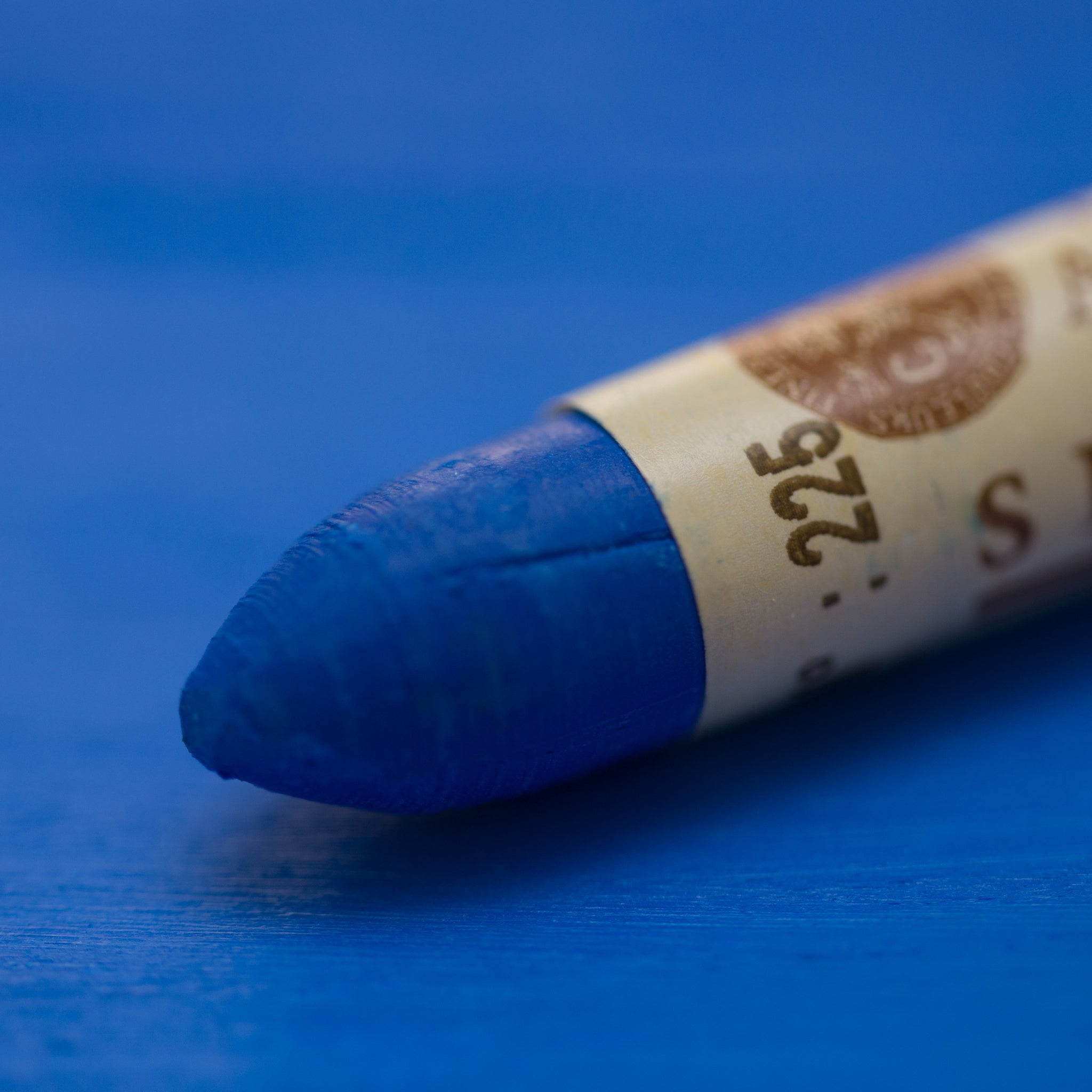 A close-up of a Sennelier oil pastel on a  blue background.