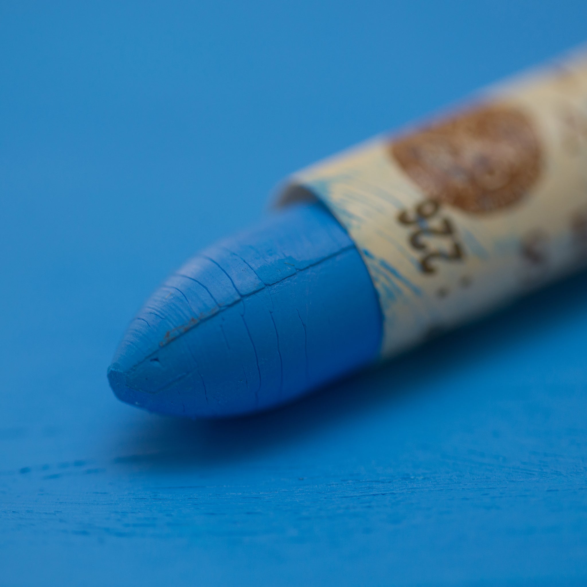 A close-up of a Sennelier oil pastel on a  blue background.