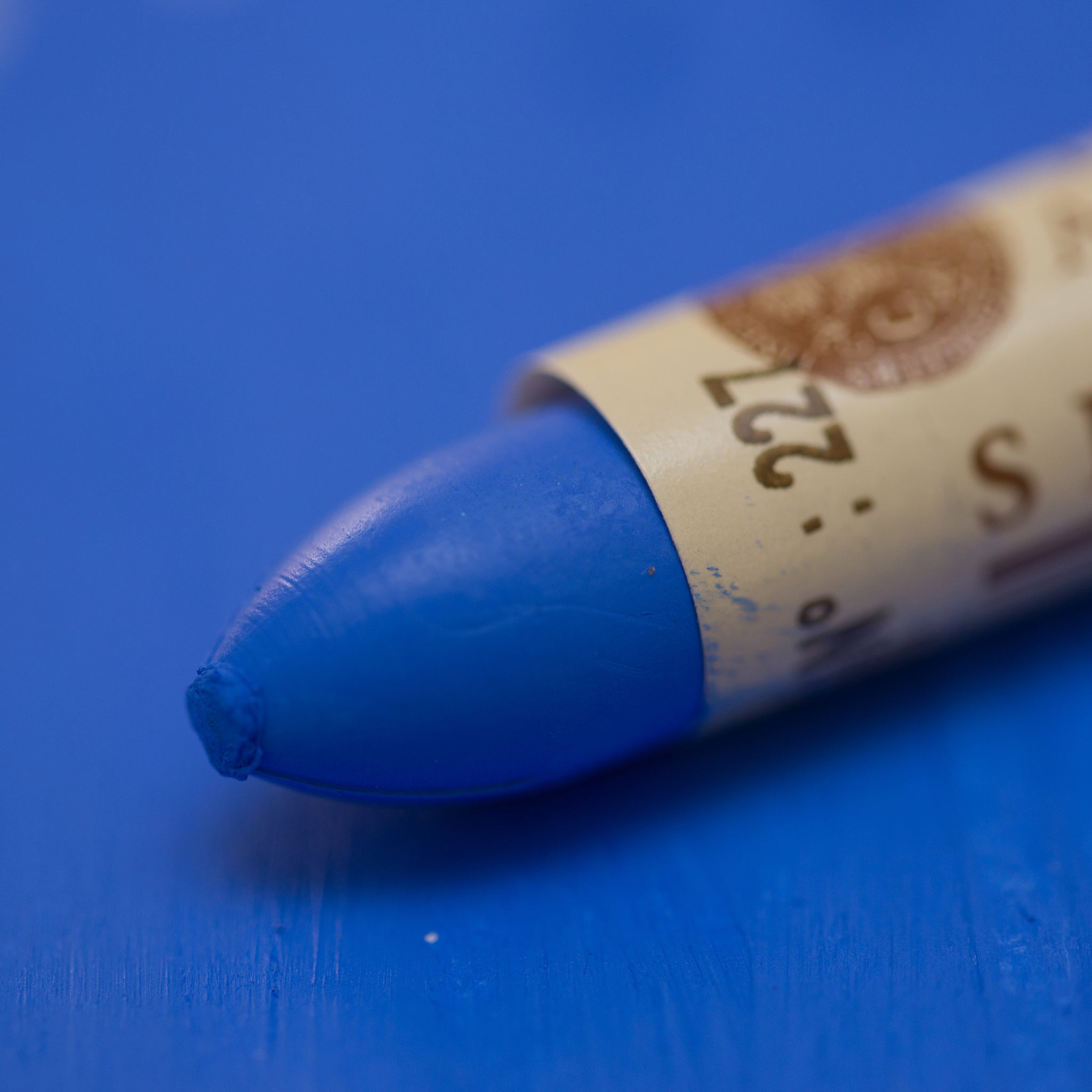 A close-up of a Sennelier oil pastel on a blue background.