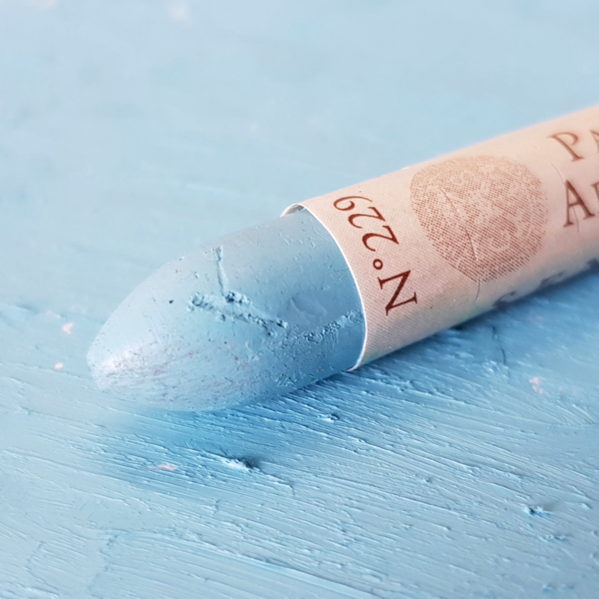 A close-up of a Sennelier oil pastel on a  blue background.