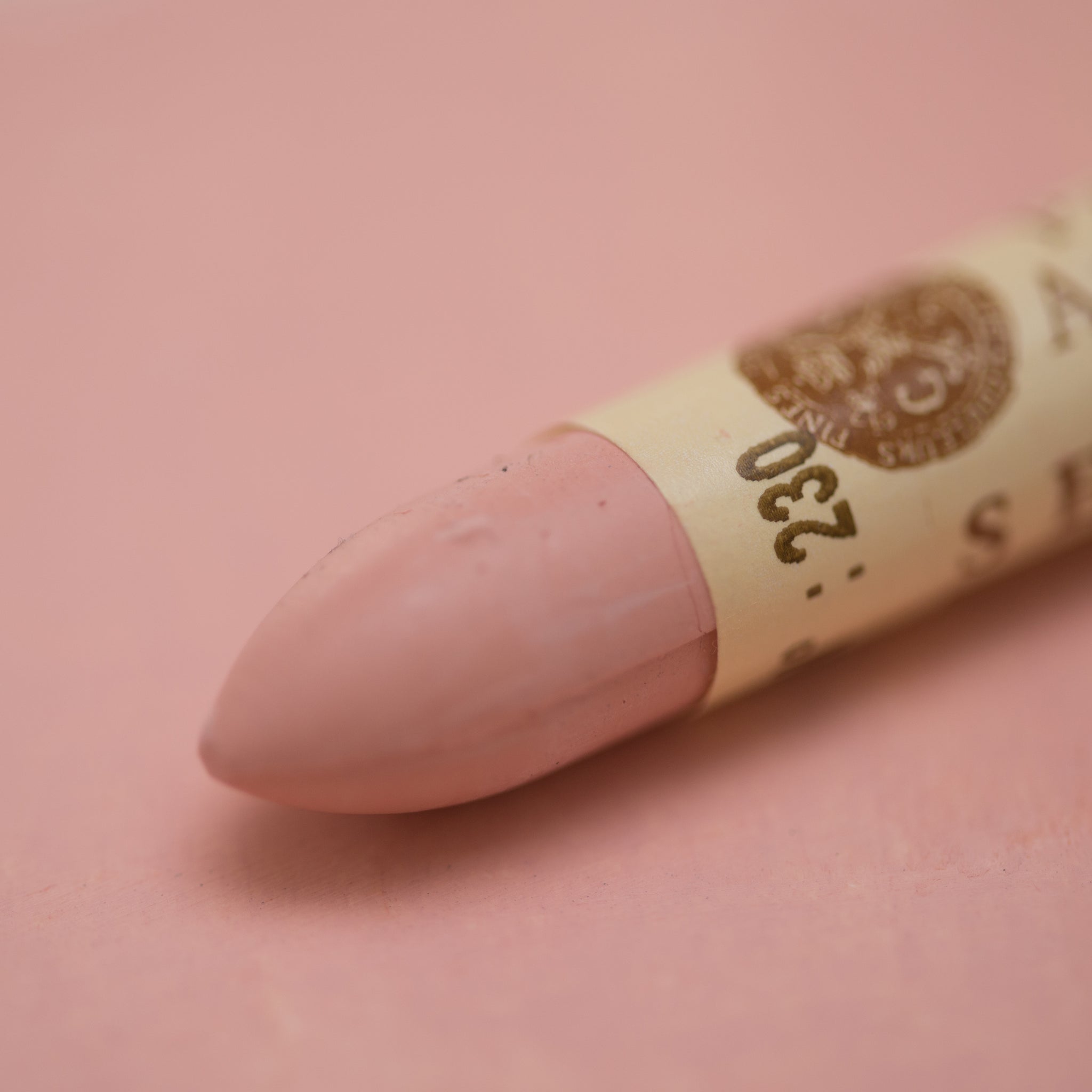 A close-up of a Sennelier oil pastel on a  pink background.
