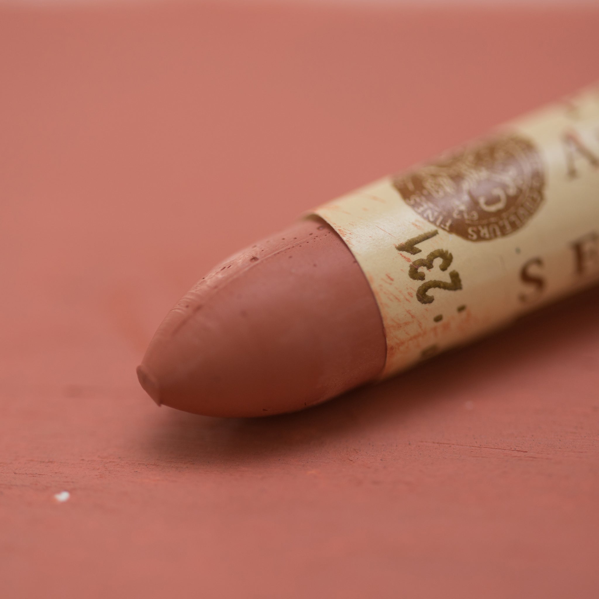 A close-up of a Sennelier oil pastel on a  red brown background.