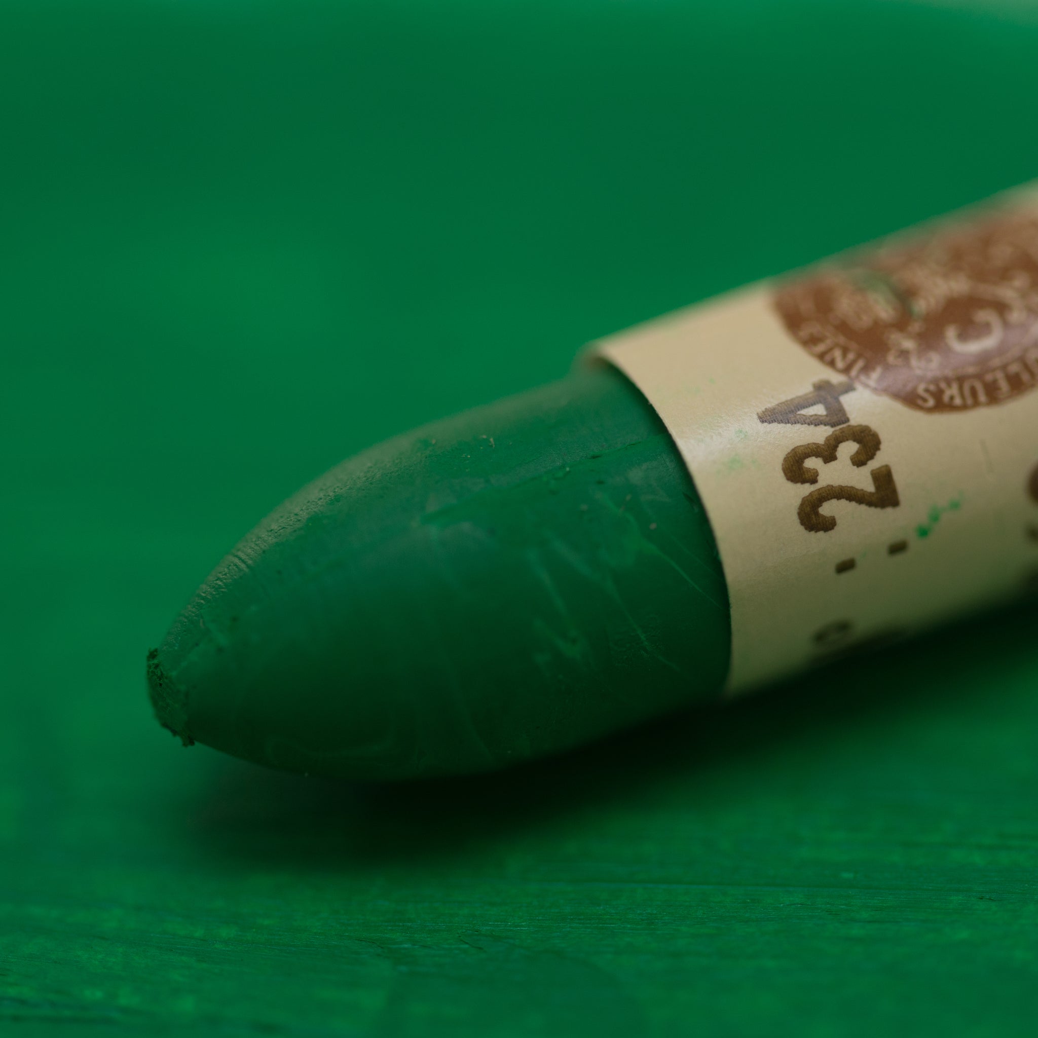 A close-up of a Sennelier oil pastel on a green background.