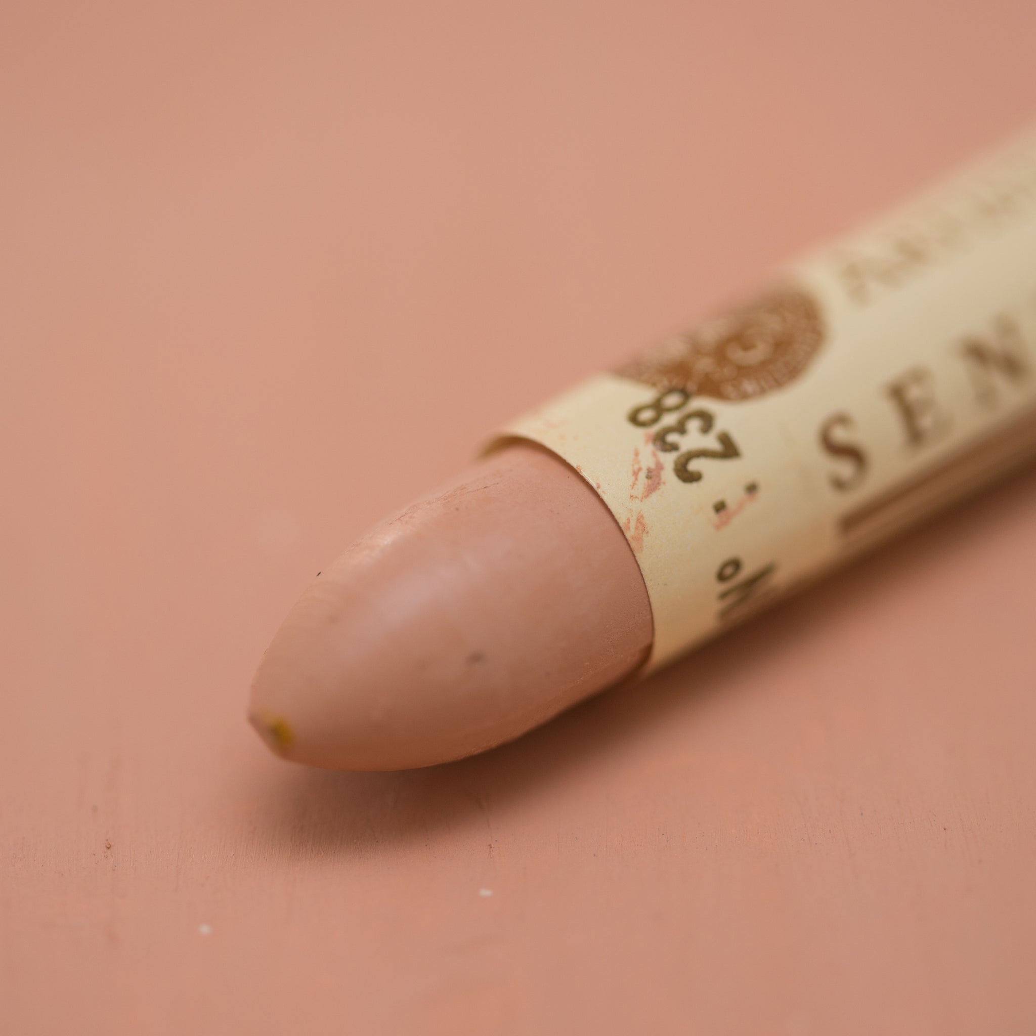 A close-up of a Sennelier oil pastel on a pink background.