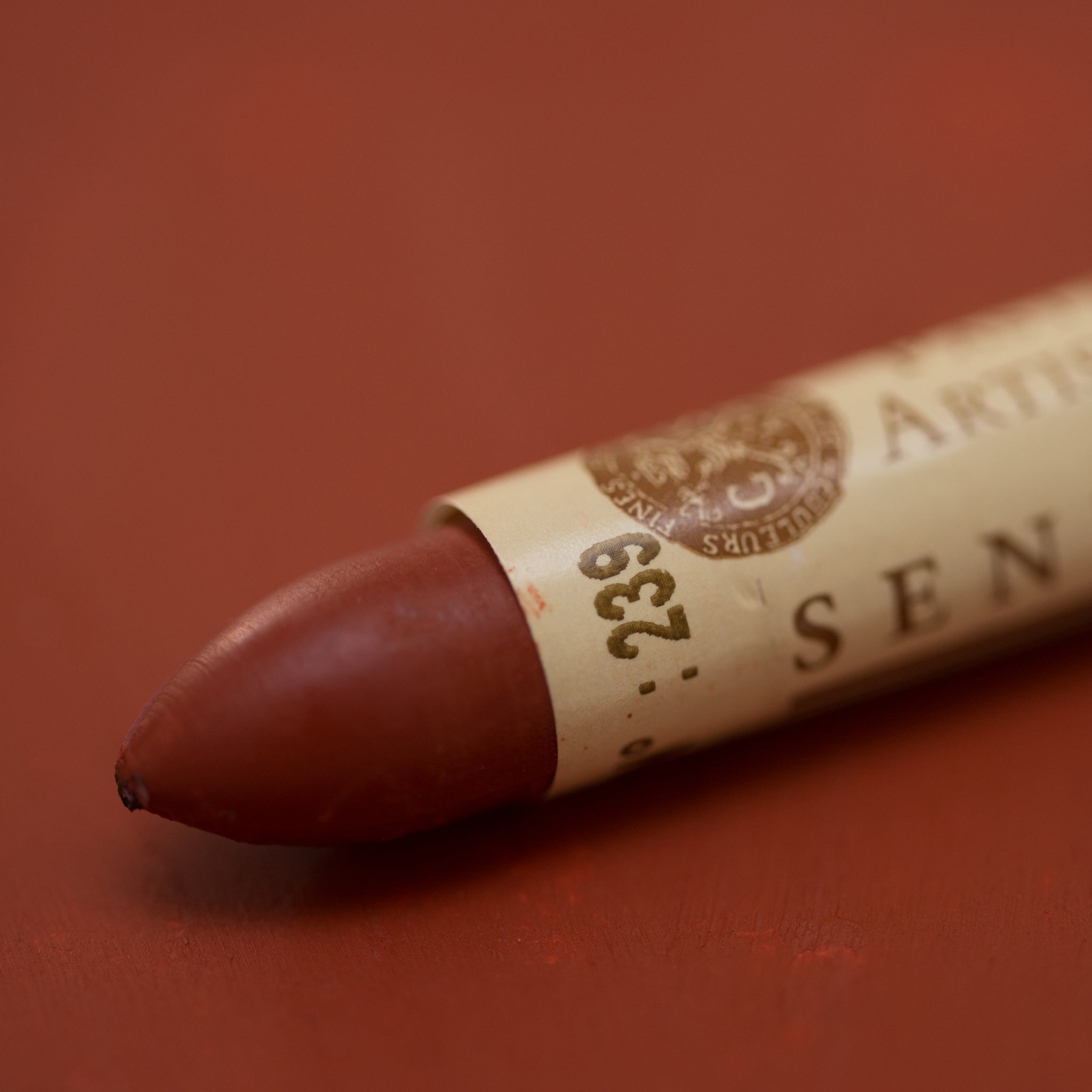 A close-up of a Sennelier oil pastel on a brown background.