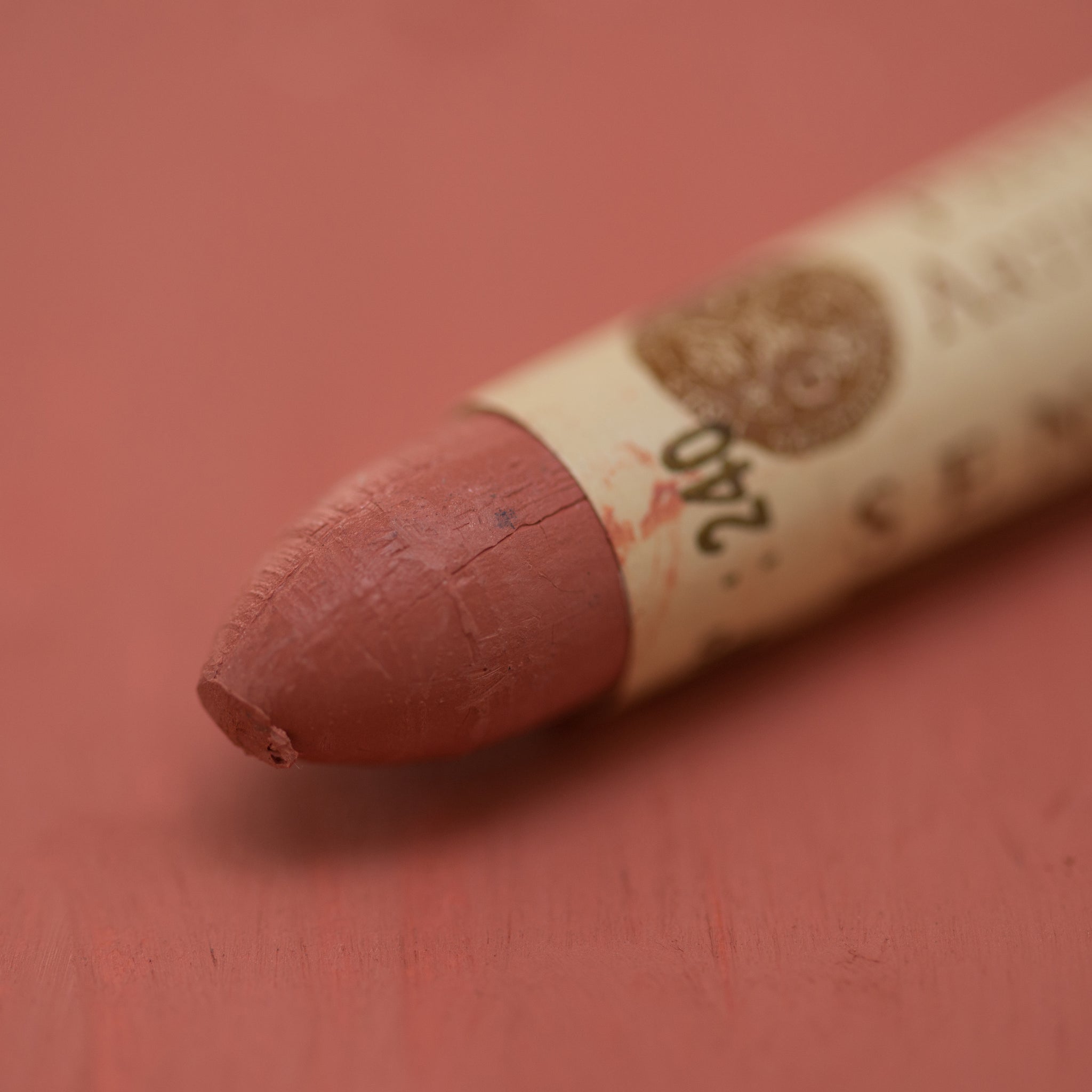 A close-up of a Sennelier oil pastel on a red brown background.