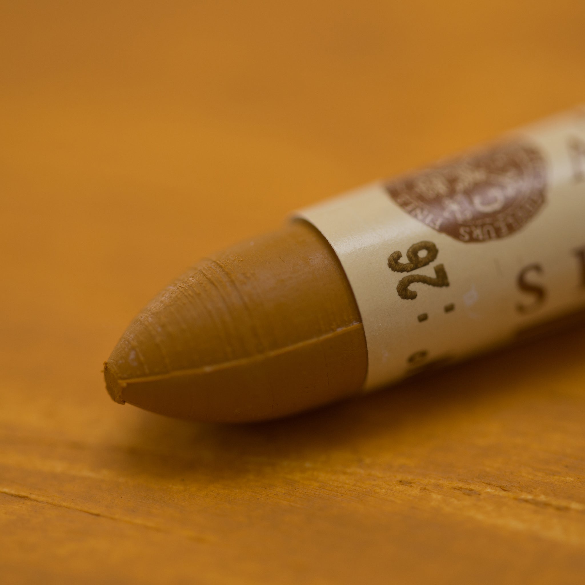 A close-up of a Sennelier oil pastel on a brown background.