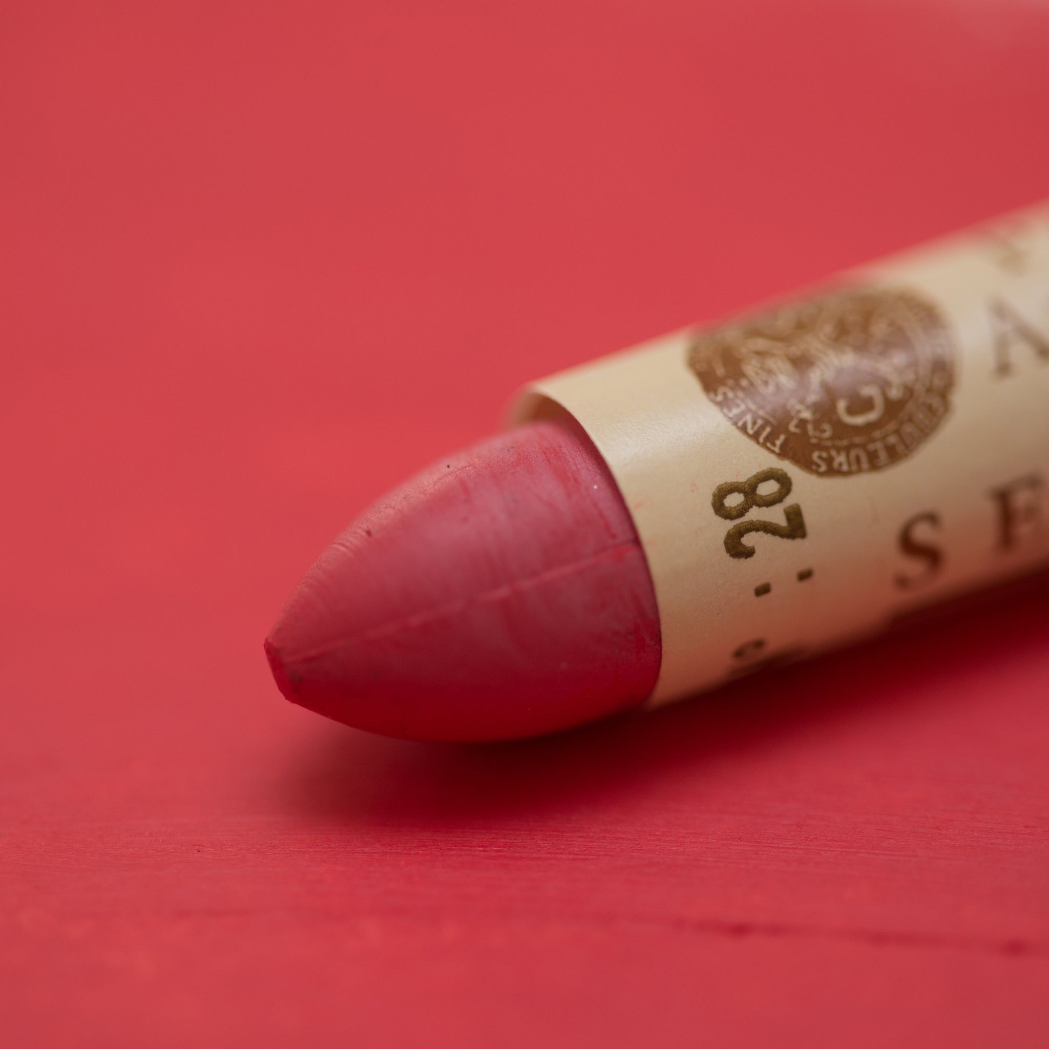 A close-up of a Sennelier oil pastel on a red background.