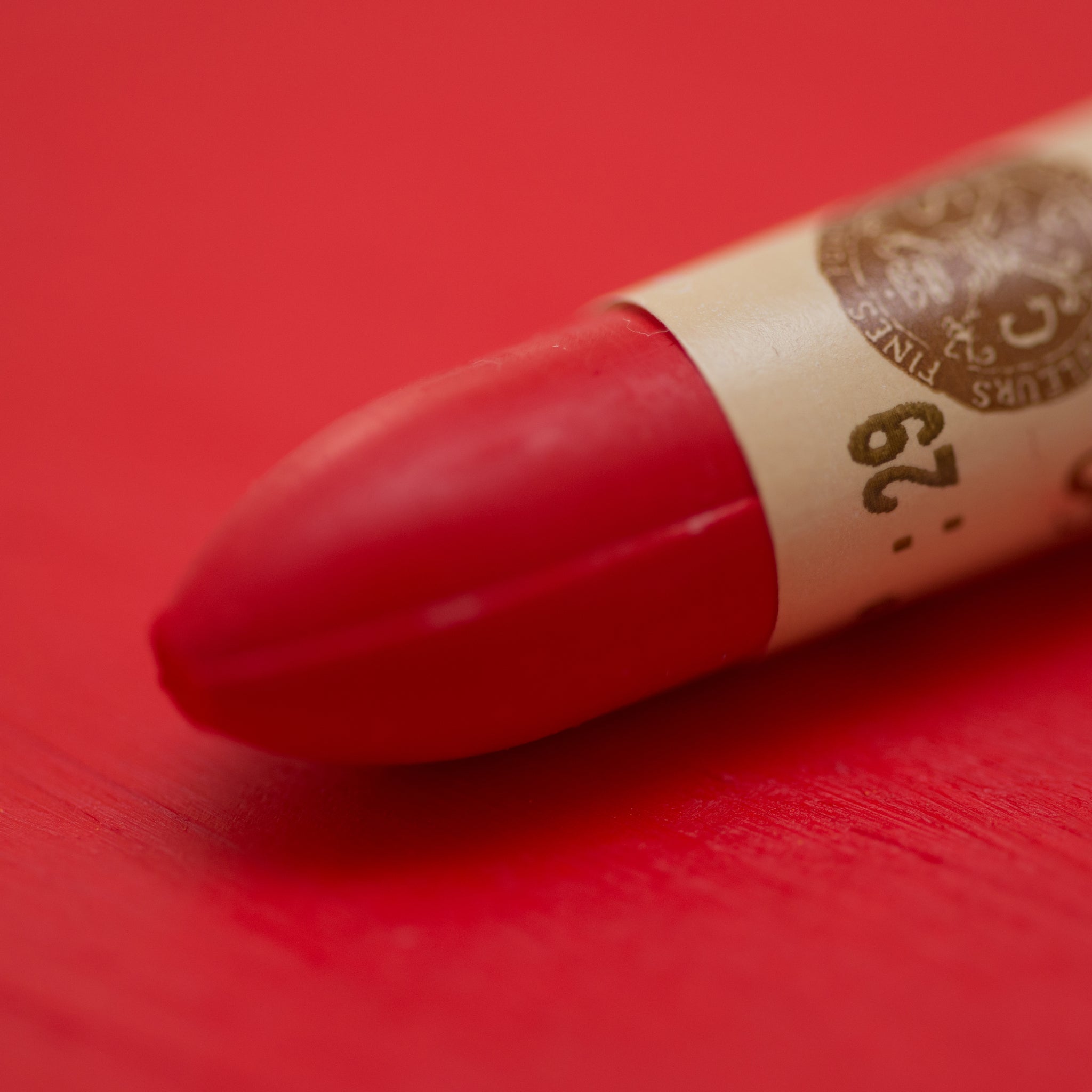 A close-up of a Sennelier oil pastel on a red background.