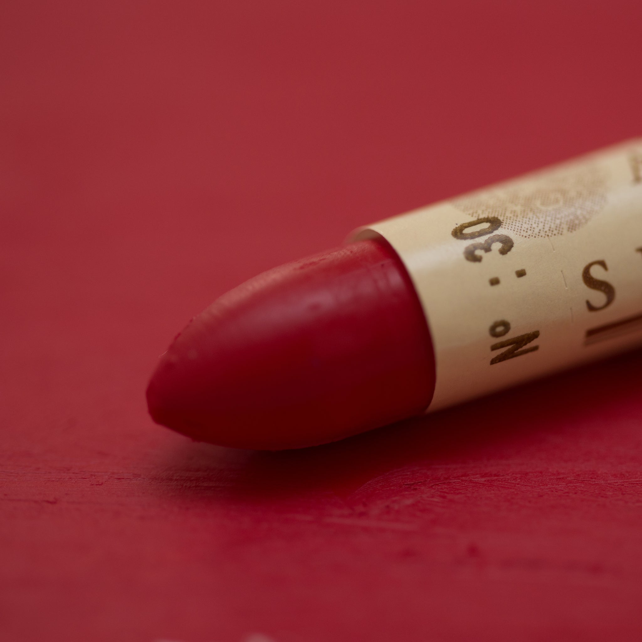 A close-up of a Sennelier oil pastel on a red background.