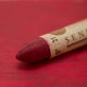 A close-up of a Sennelier oil pastel on a red background.