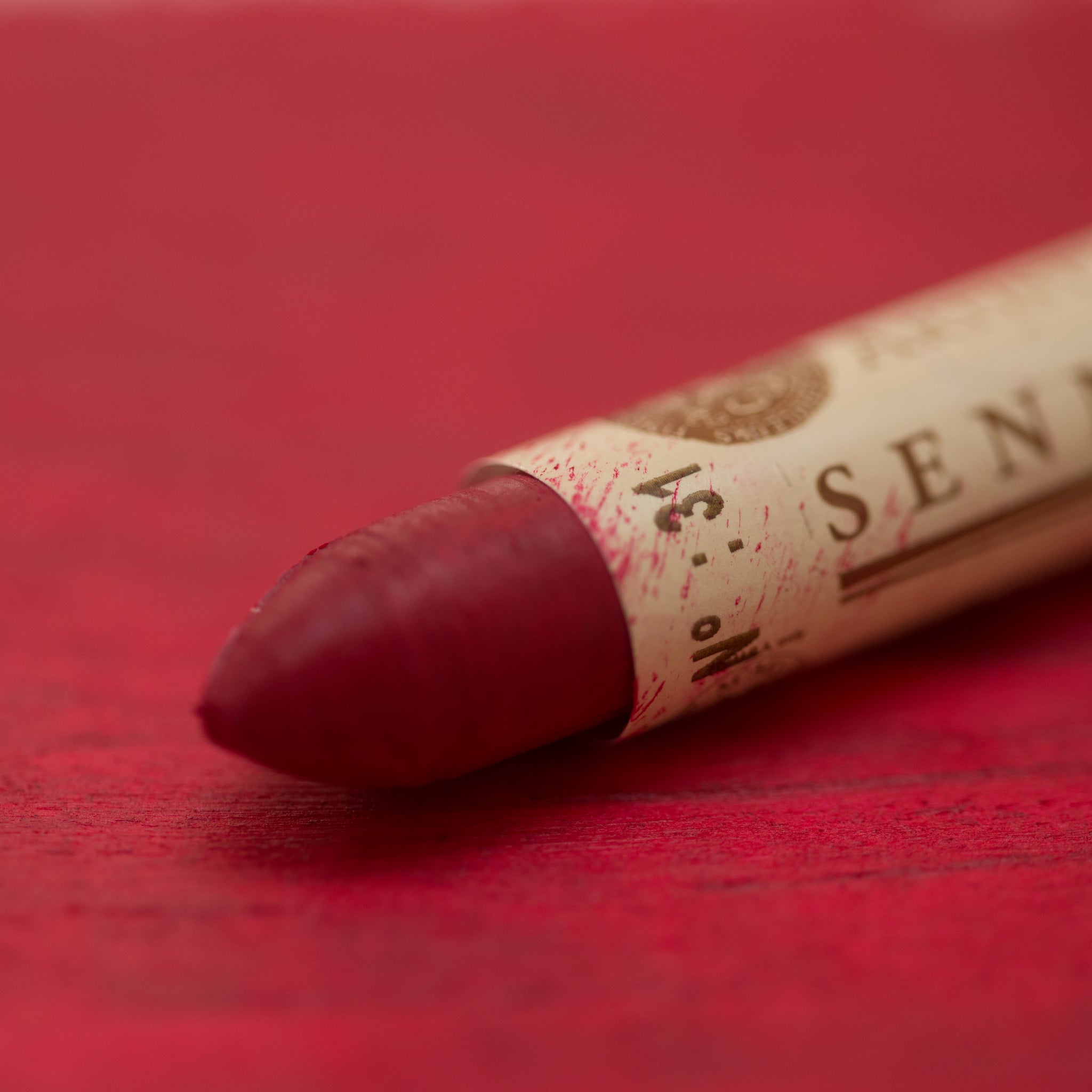 A close-up of a Sennelier oil pastel on a red background.