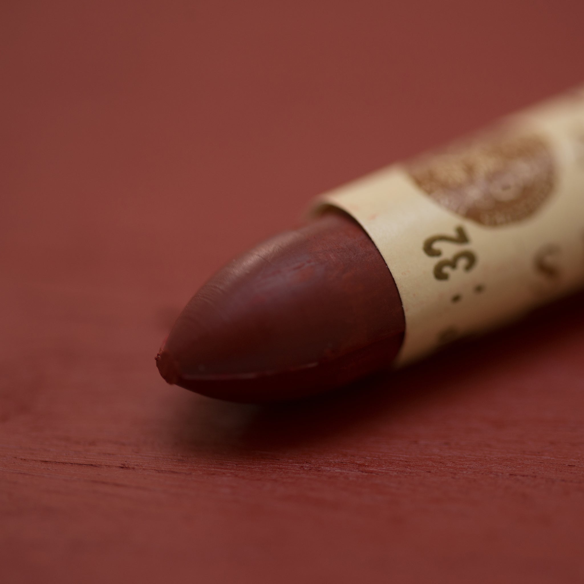 A close-up of a Sennelier oil pastel on a brown-red background.