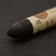 A close-up of a Sennelier oil pastel on a brown background.