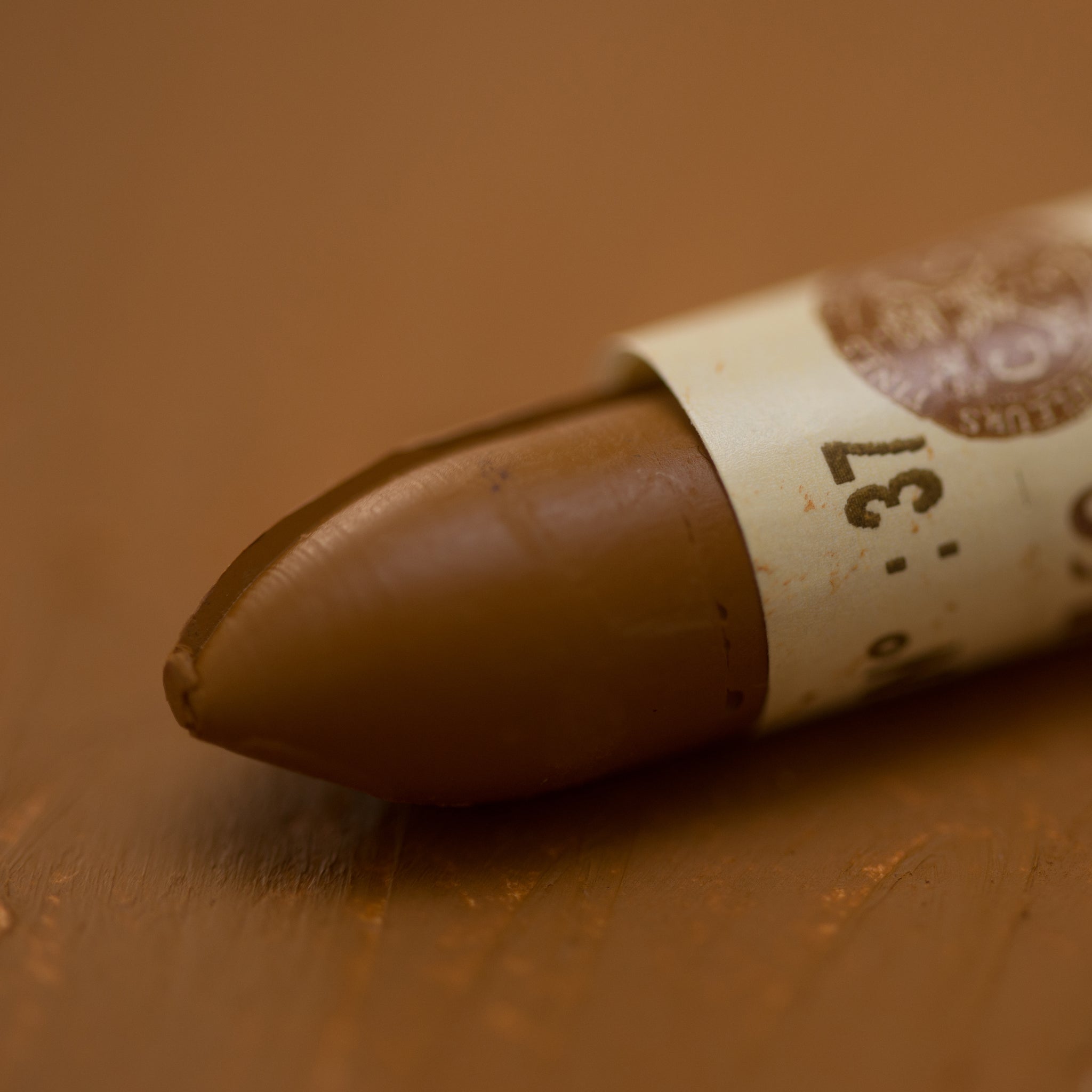 A close-up of a Sennelier oil pastel on a brown background.