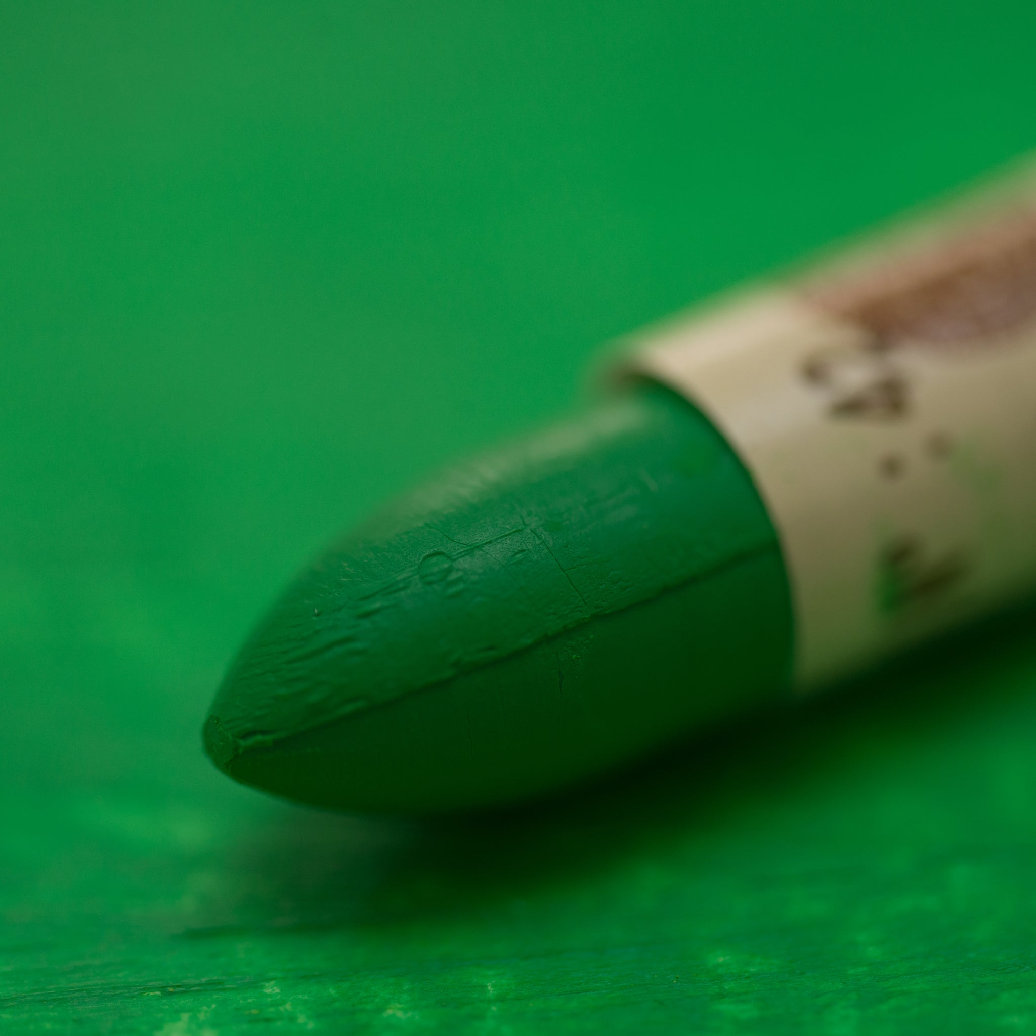 A close-up of a Sennelier oil pastel on a green background.