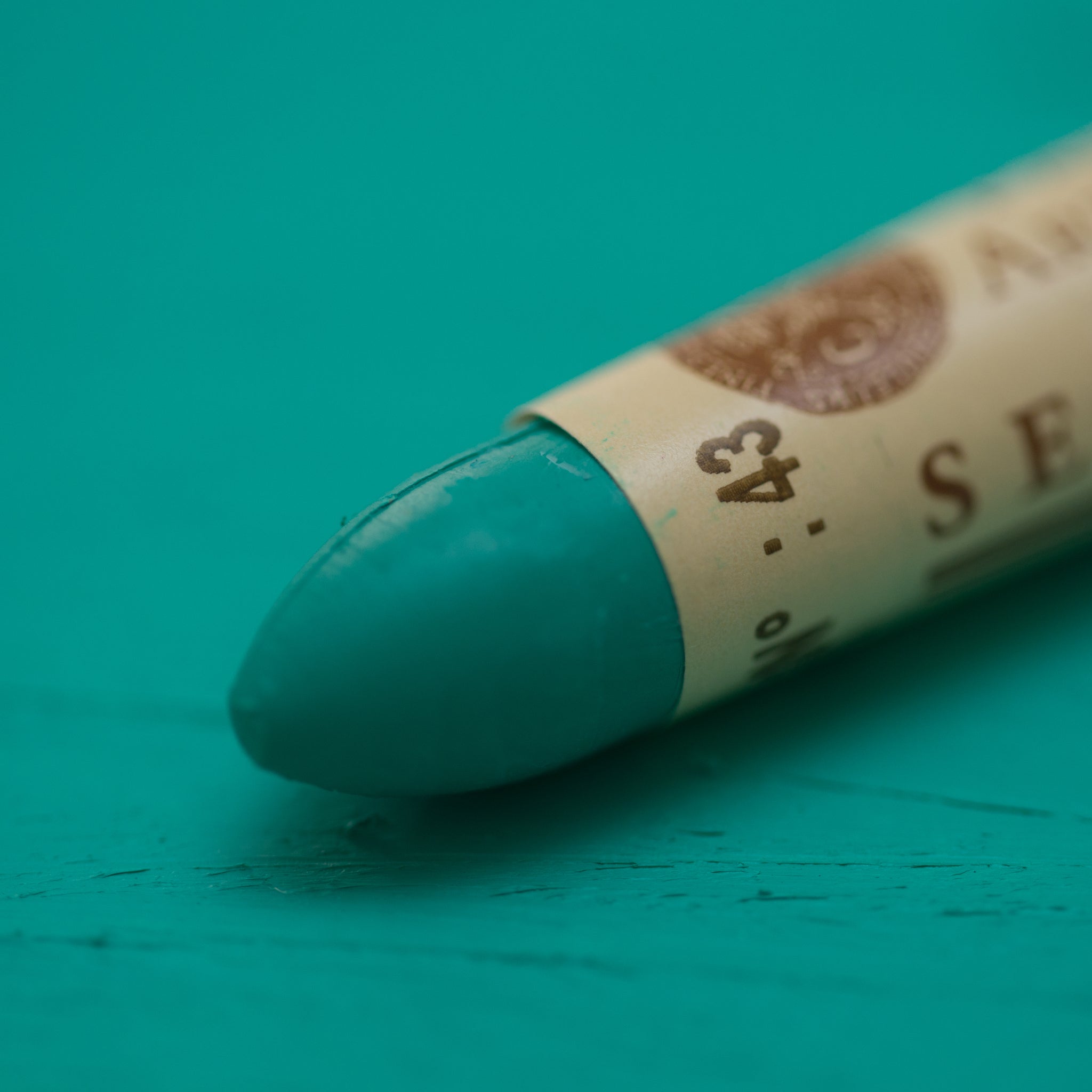 A close-up of a Sennelier oil pastel on a green background.