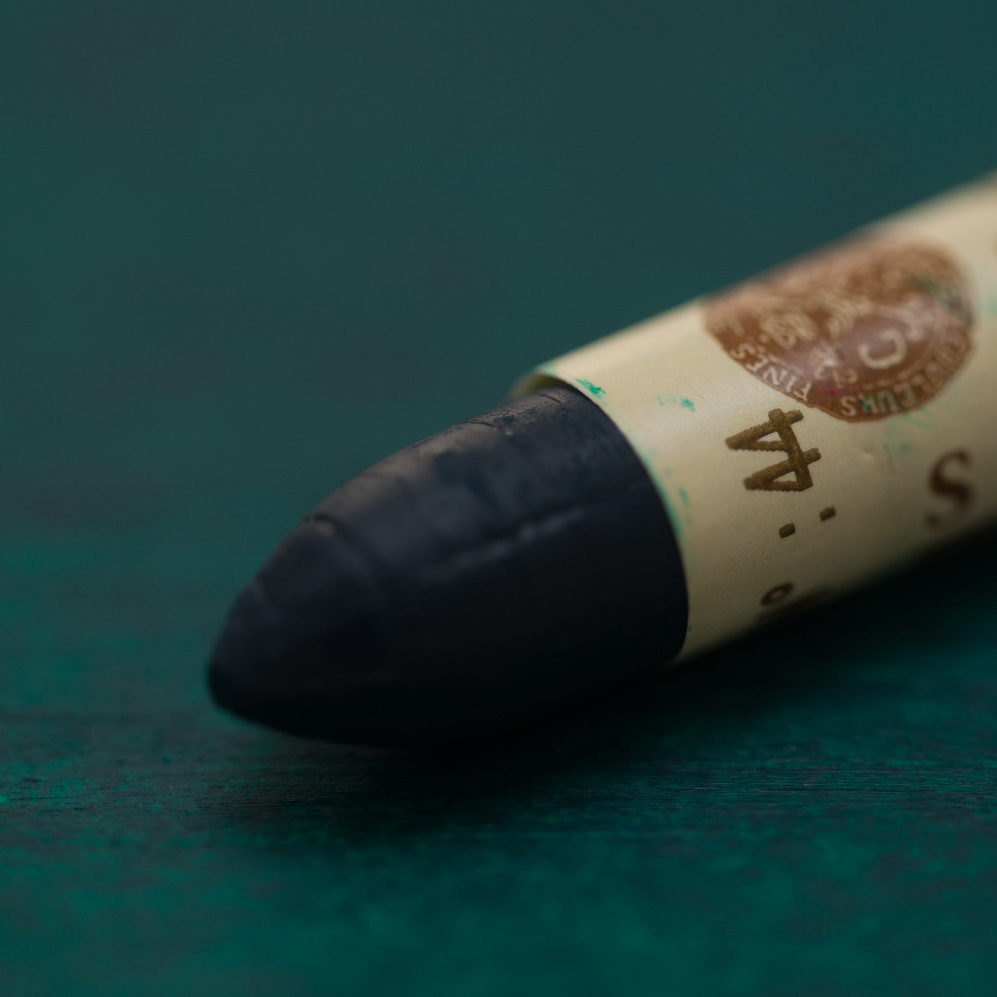 A close-up of a Sennelier oil pastel on a green background.