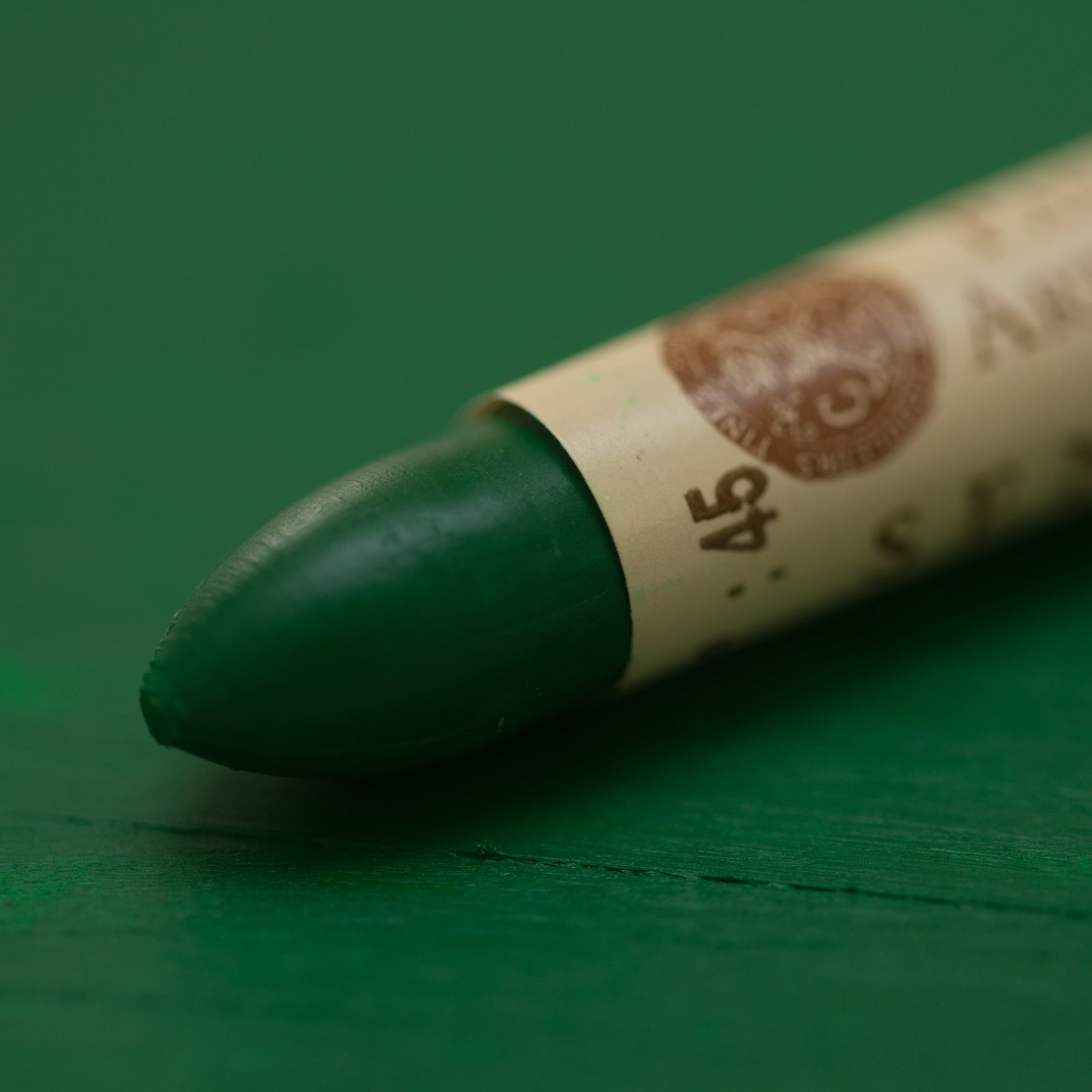 A close-up of a Sennelier oil pastel on a green background.