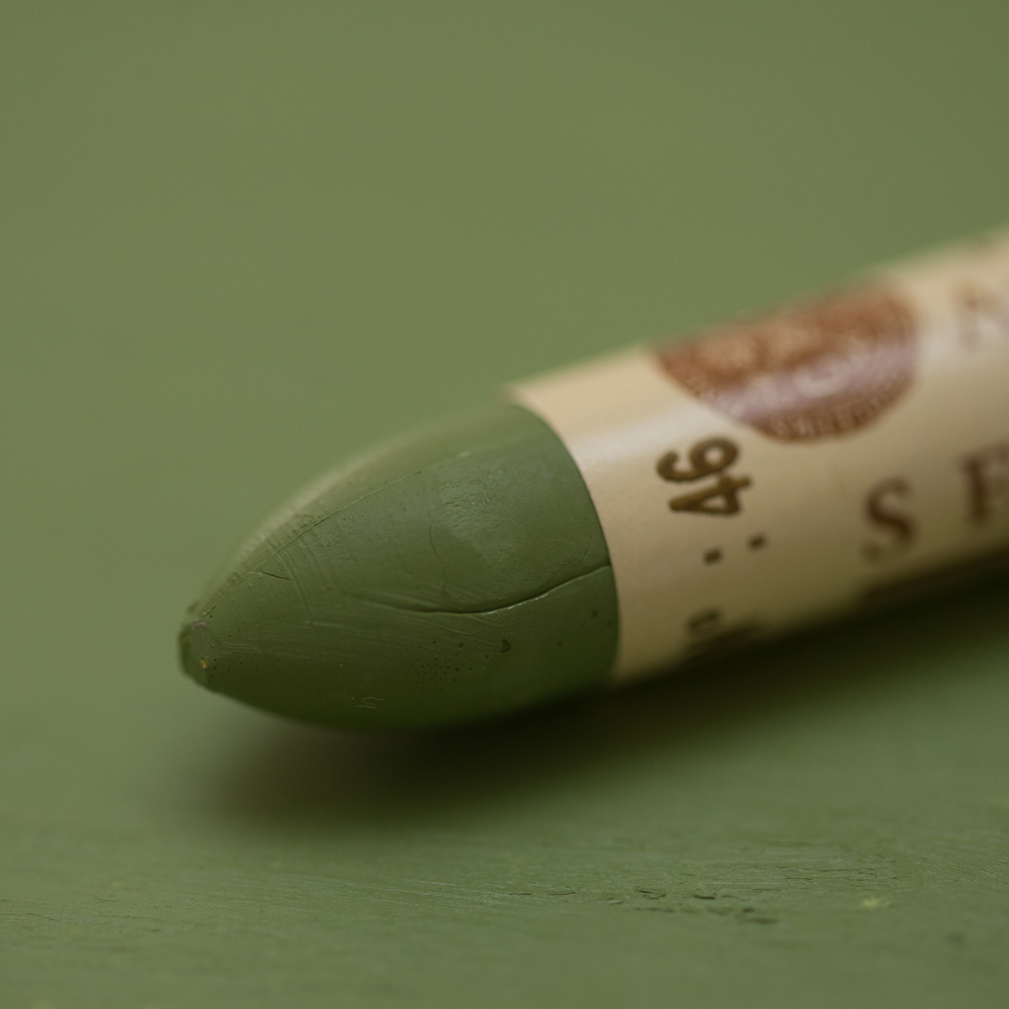A close-up of a Sennelier oil pastel on a green background.