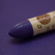 A close-up of a Sennelier oil pastel on a purple background.