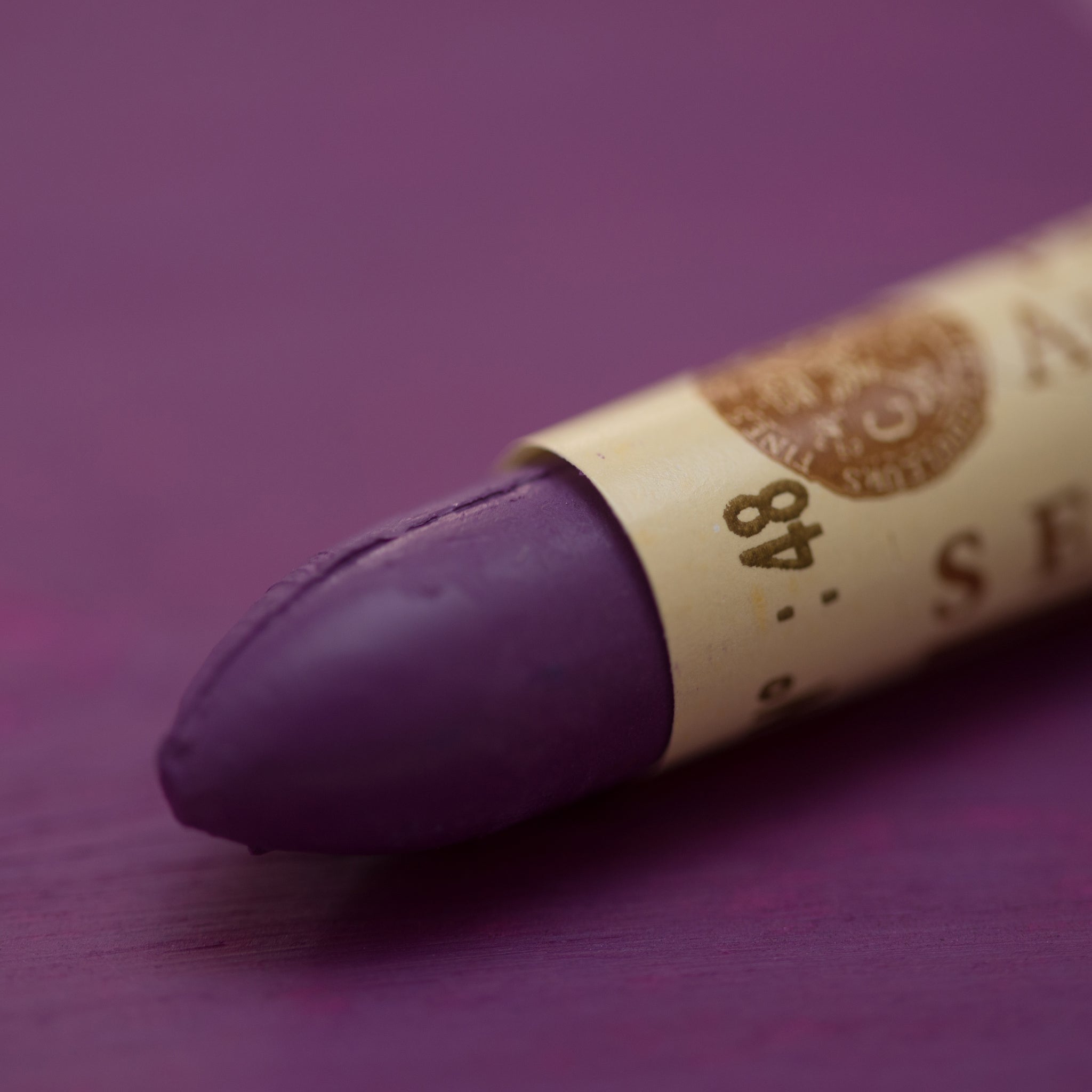 A close-up of a Sennelier oil pastel on a purple background.