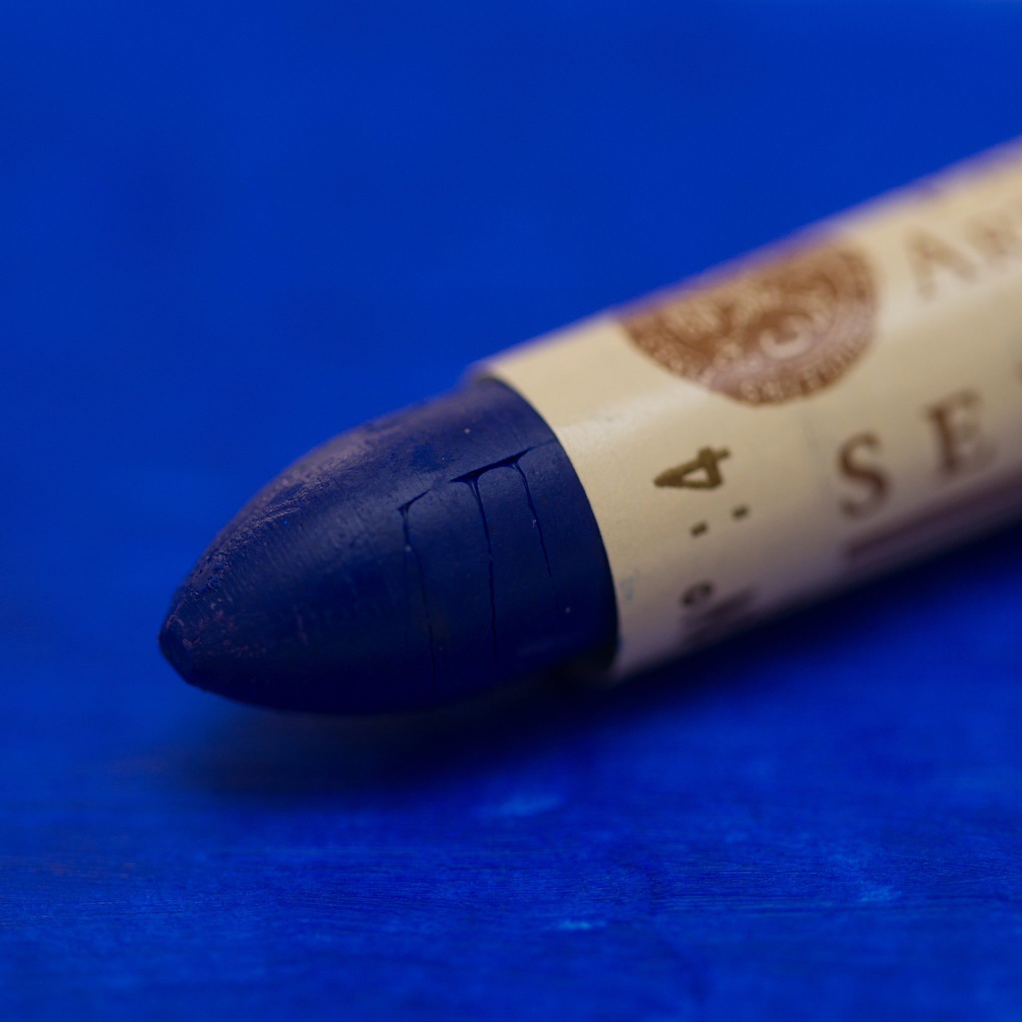 A close-up of a Sennelier oil pastel on a blue background.