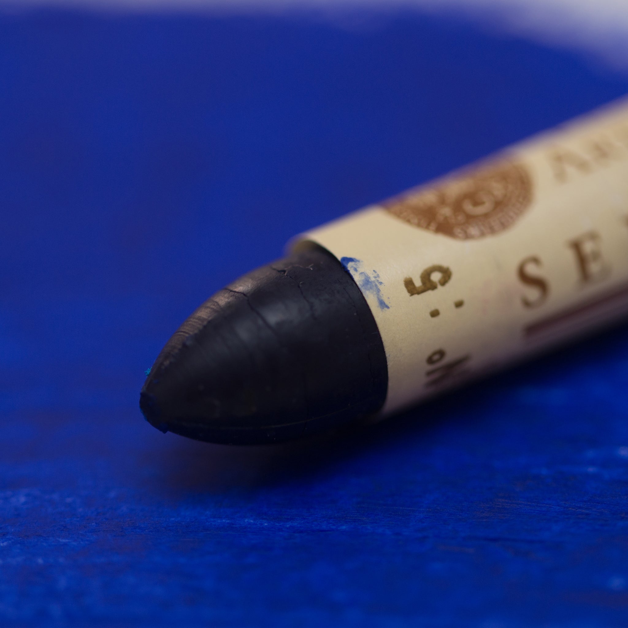 A close-up of a Sennelier oil pastel on a blue background.