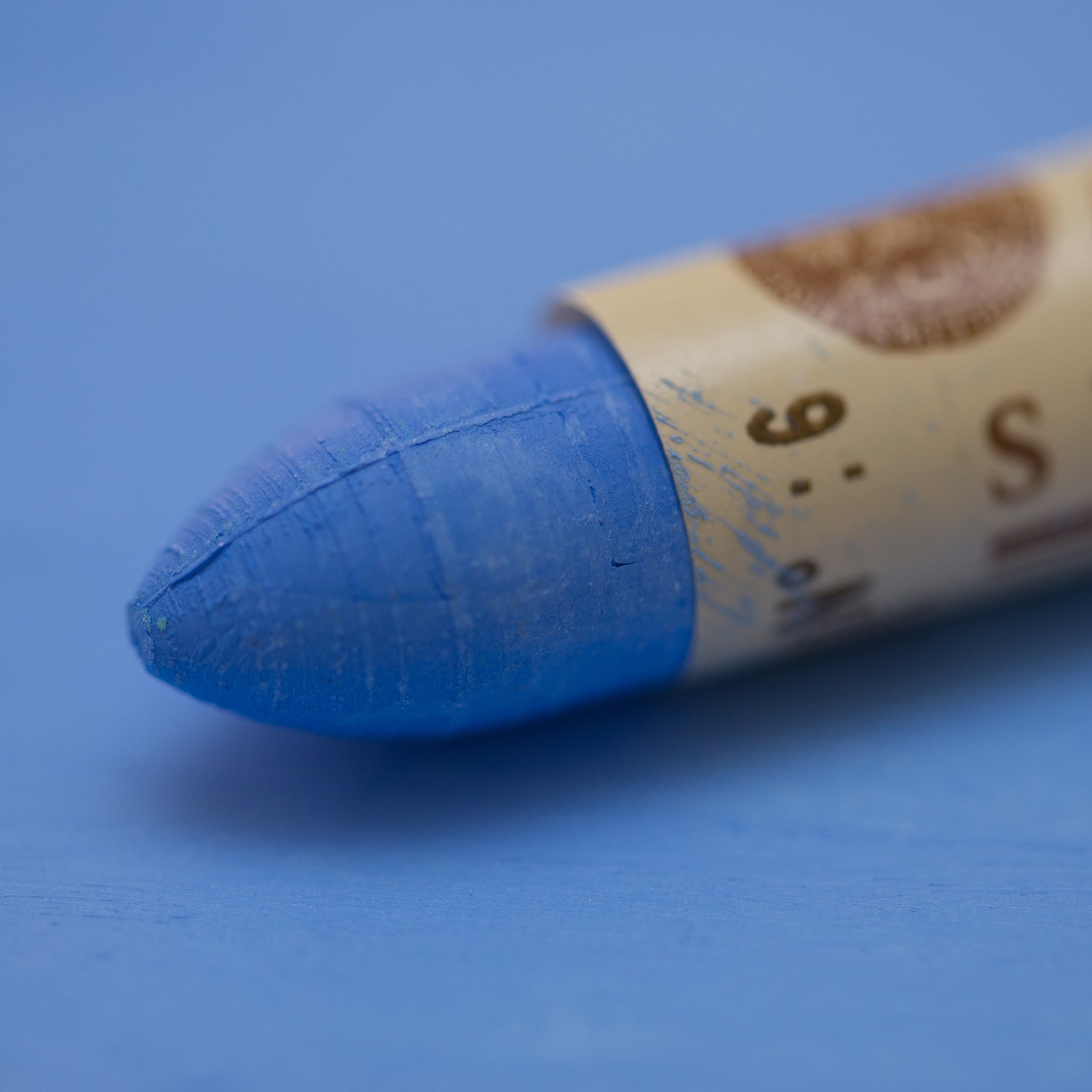 A close-up of a Sennelier oil pastel on a blue background.