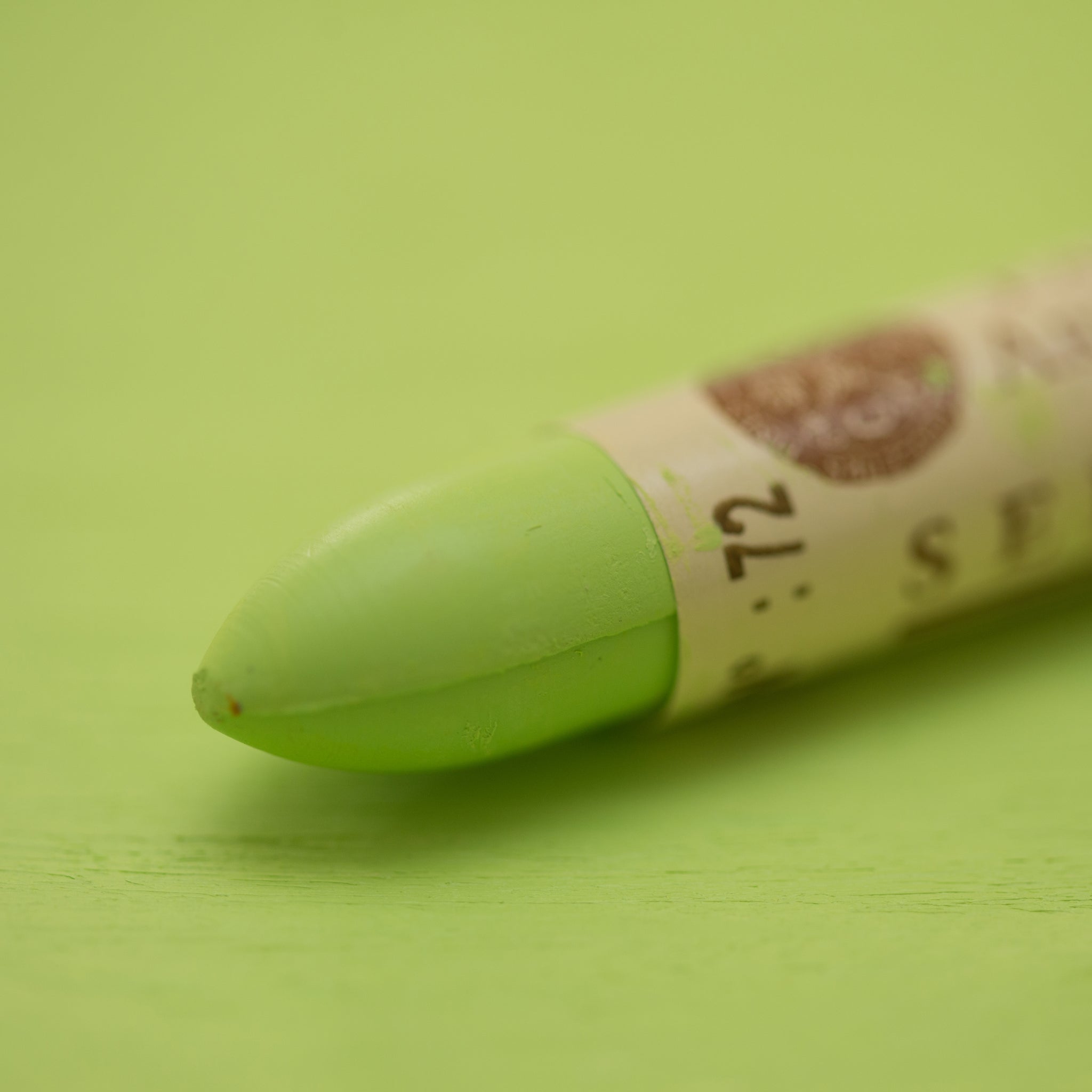 A close-up of a Sennelier oil pastel on a green background.