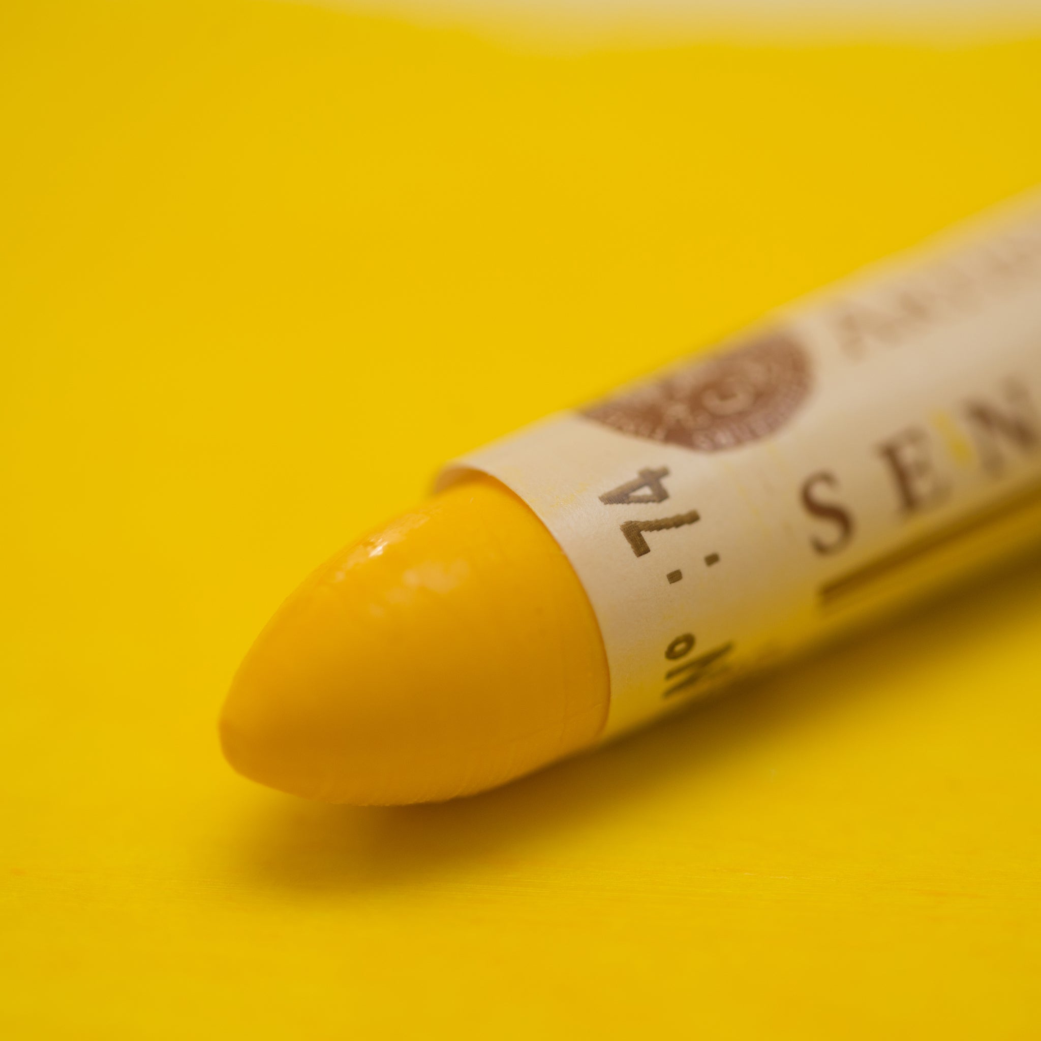 A close-up of a Sennelier oil pastel on a yellow background.