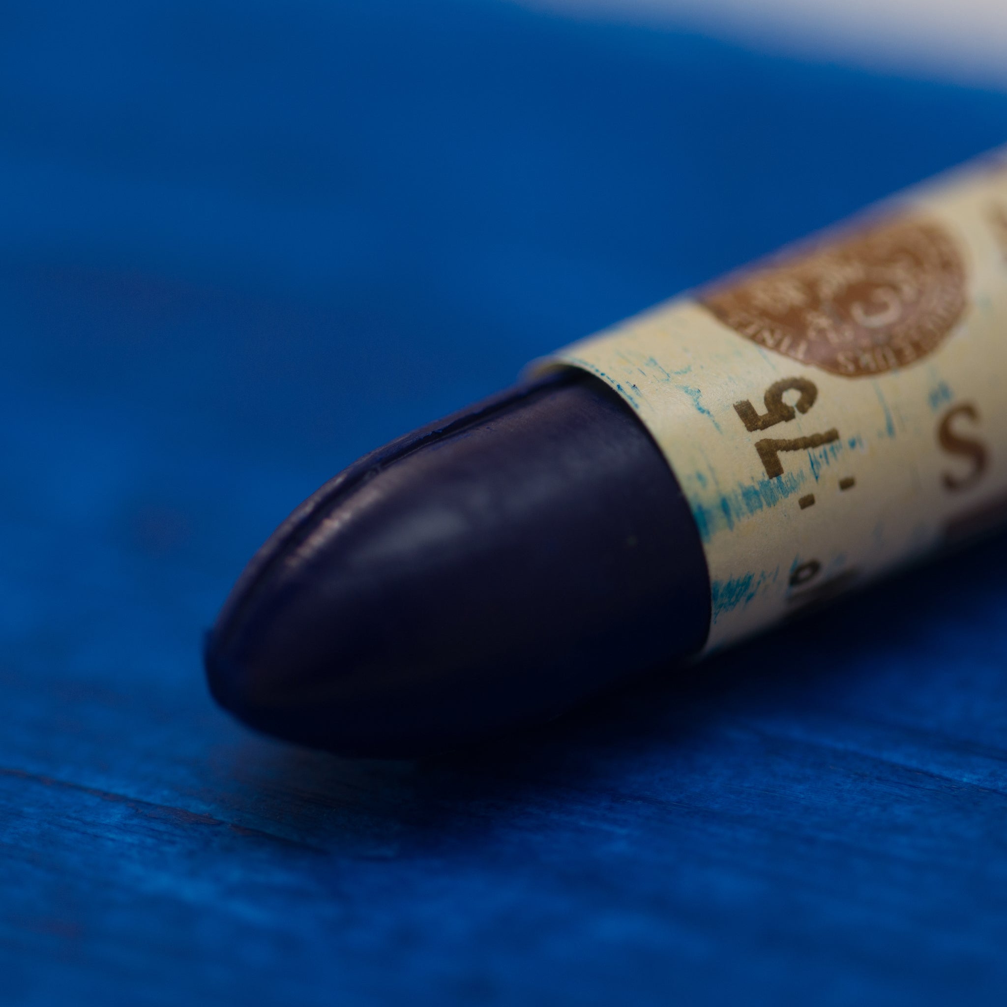 A close-up of a Sennelier oil pastel on a blue background.